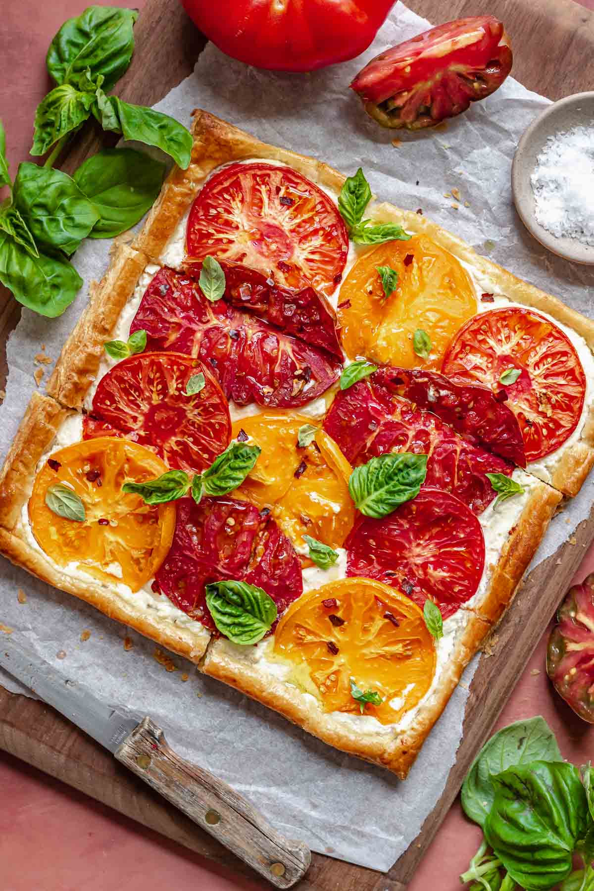 Tomato tart finished with basil, olive oil, flaky salt, and red pepper flakes on a cutting board.