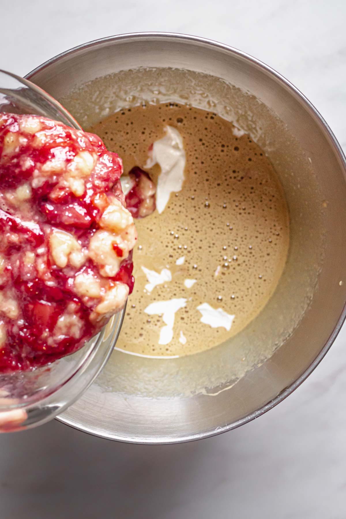 Mashed strawberries and bananas pouring into cake batter.