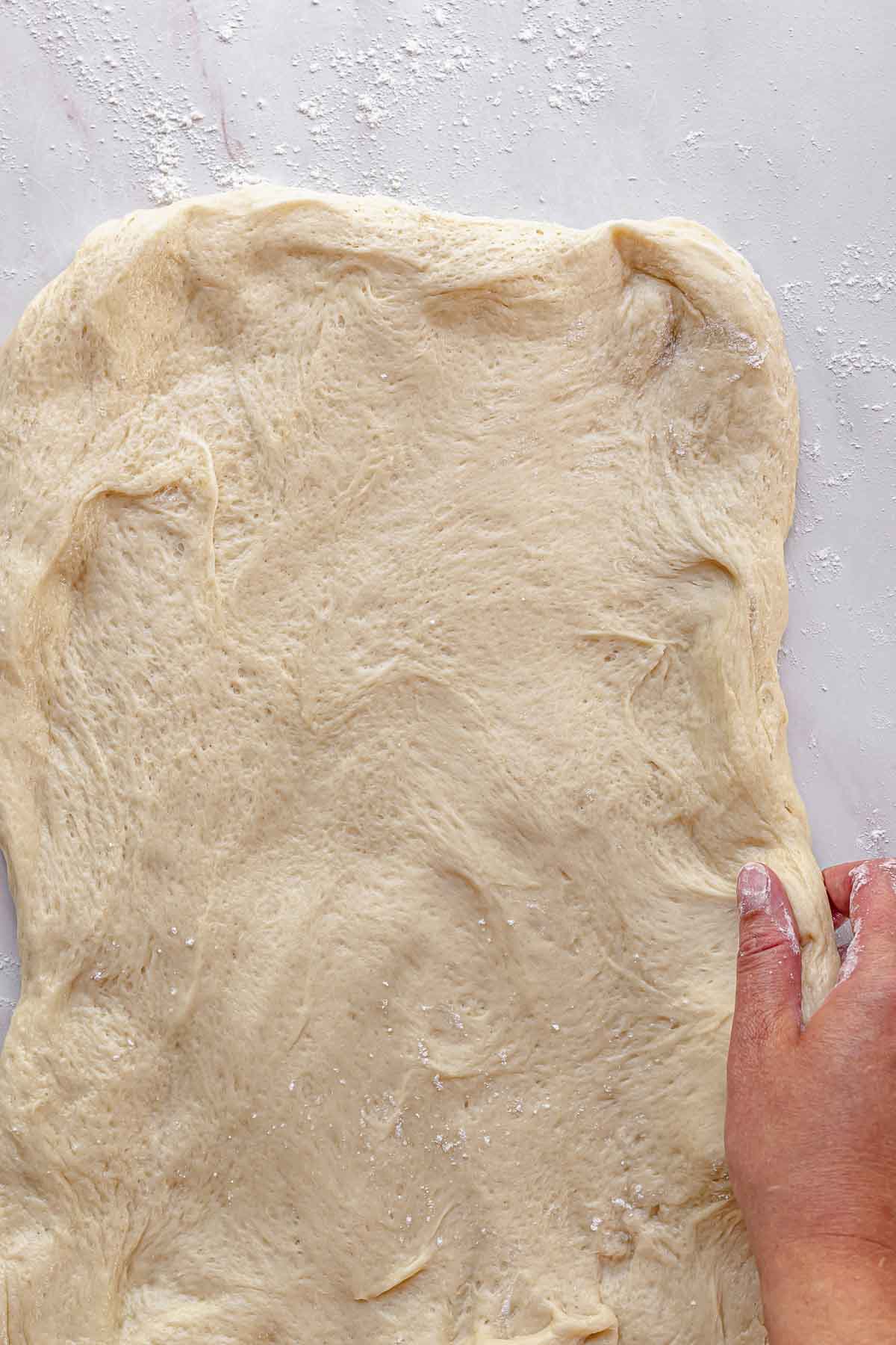 A hand stretches brioche dough on a counter into a rectangle.
