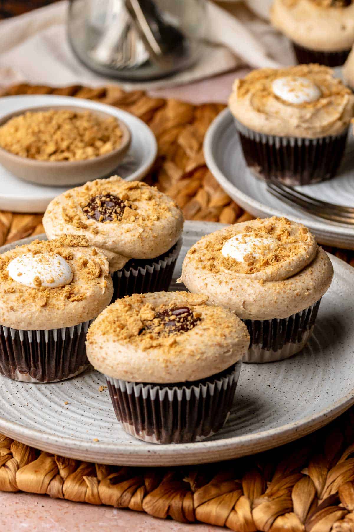 S'mores cupcakes on a plate with a bowl of graham cracker crumbs in the background.