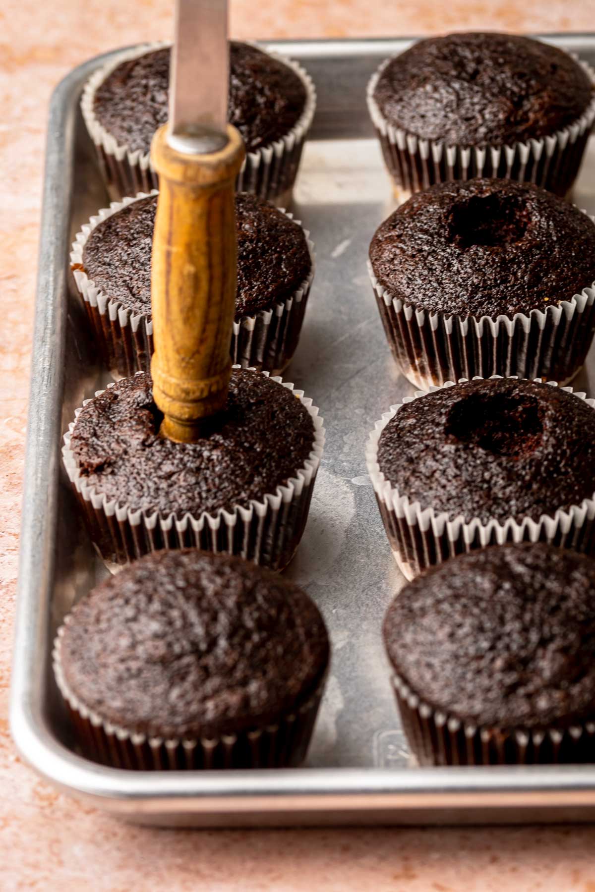 A spoon handle pushes a hole into the center of a baked cupcake.