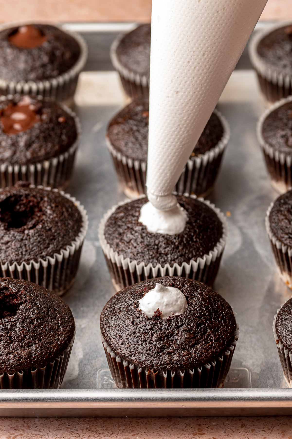 Marshmallow fluff being piped into the center of the cupcake.