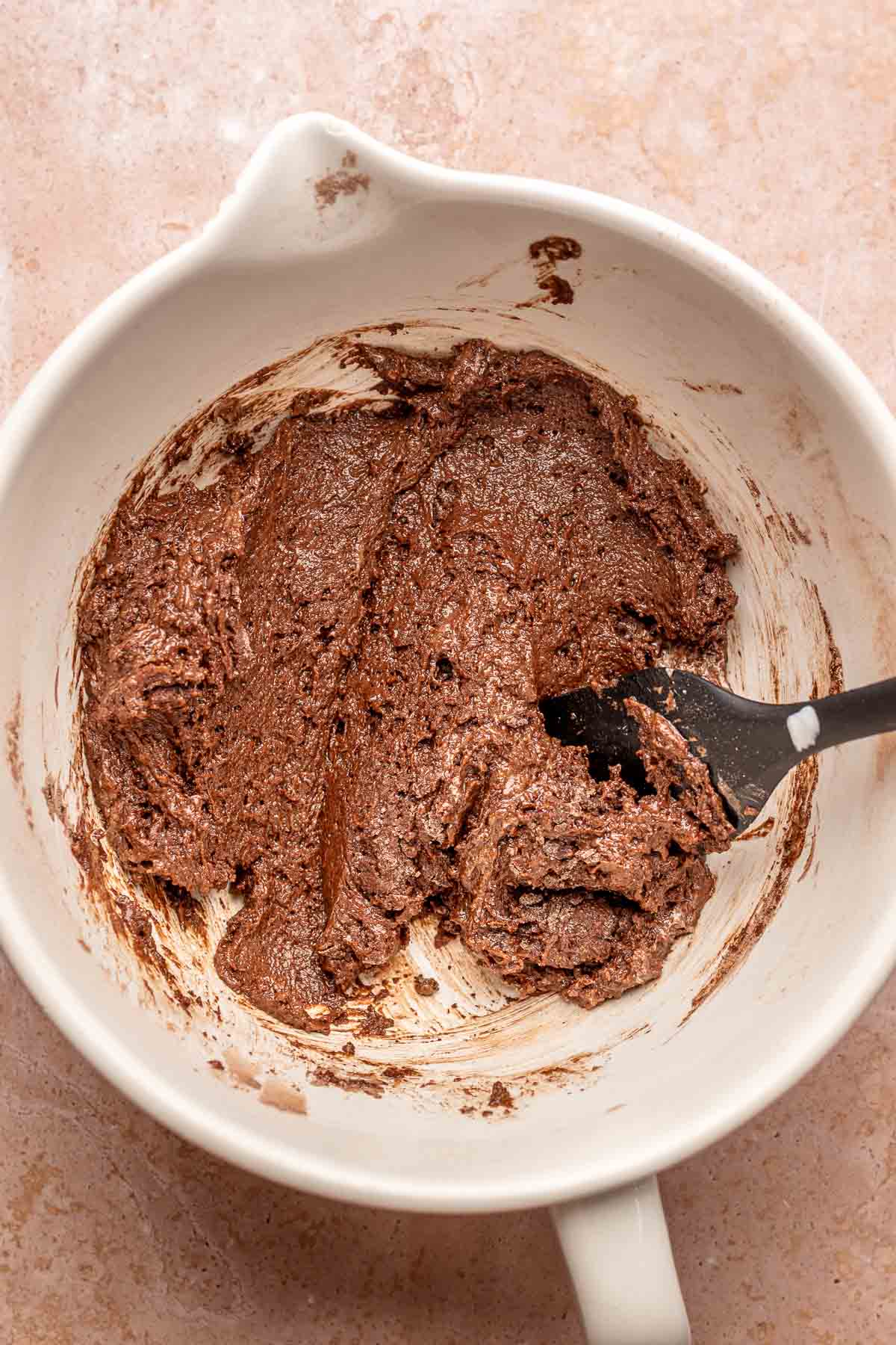 A spatula mixes chocolate cake batter in a bowl.