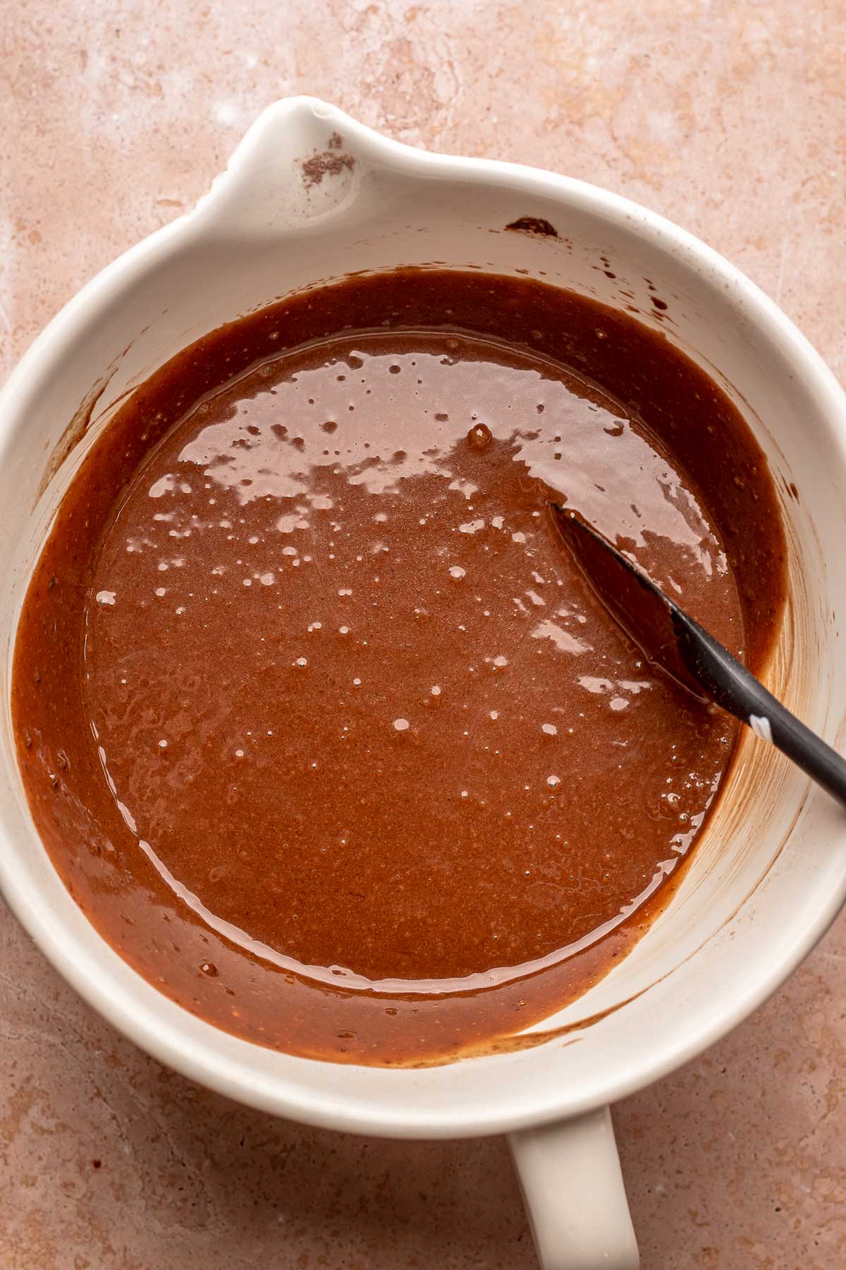 A spatula mixes chocolate cake batter in a bowl.