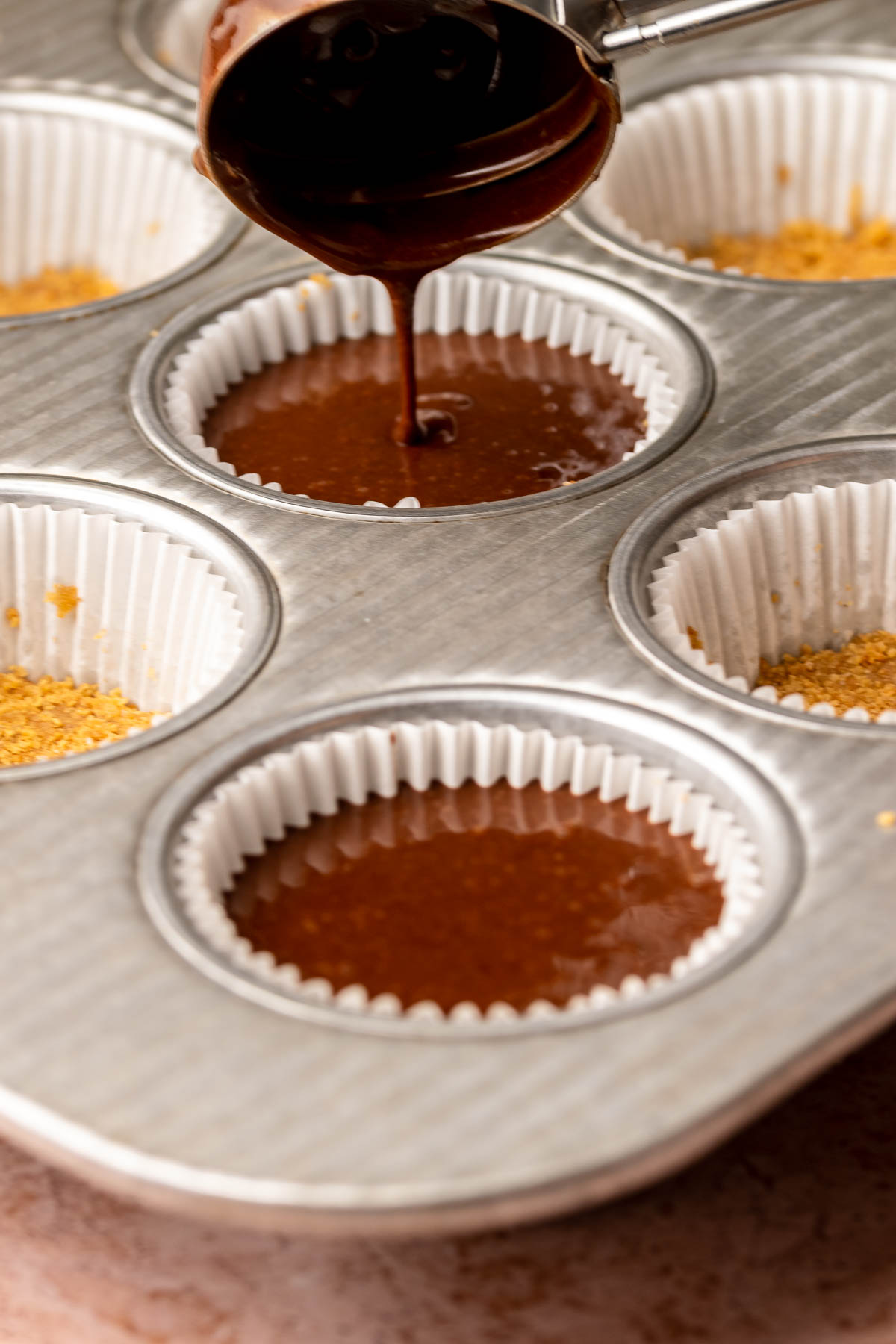 A trigger scoops adds chocolate cake batter into cupake liners.