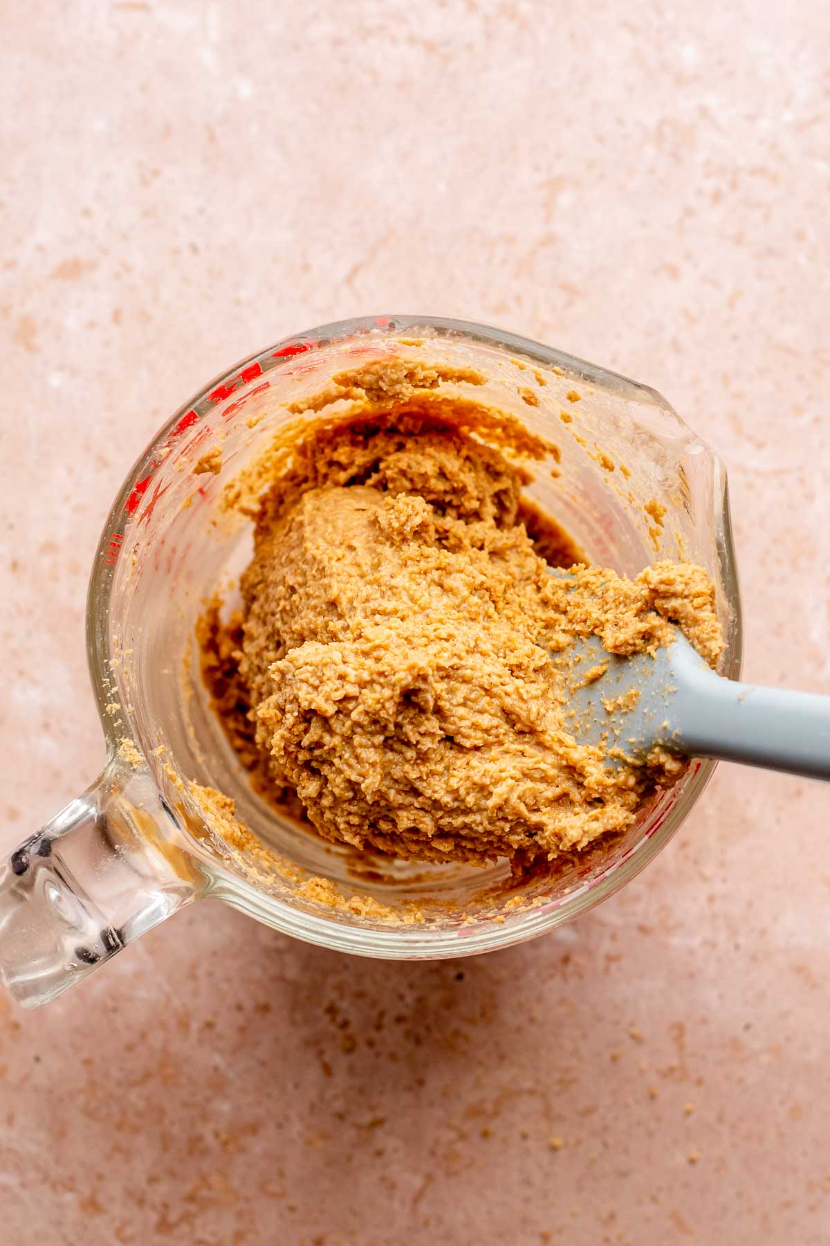 A spatula mixes graham cracker paste in a measuring cup.