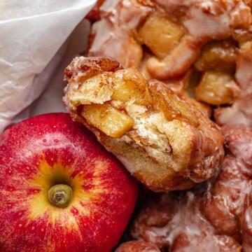 A basket of apple fritter donuts next to an apple. One it broken open.