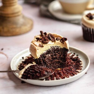 Mocha cupcake on a plate with a bite removed sitting on a spoon.