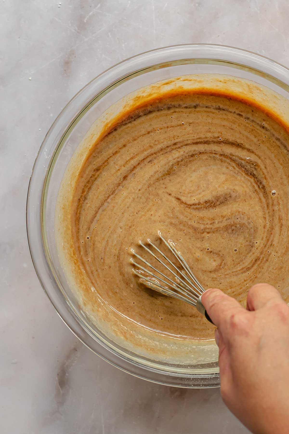 A hand whisks together ingredients for apple butter pie.