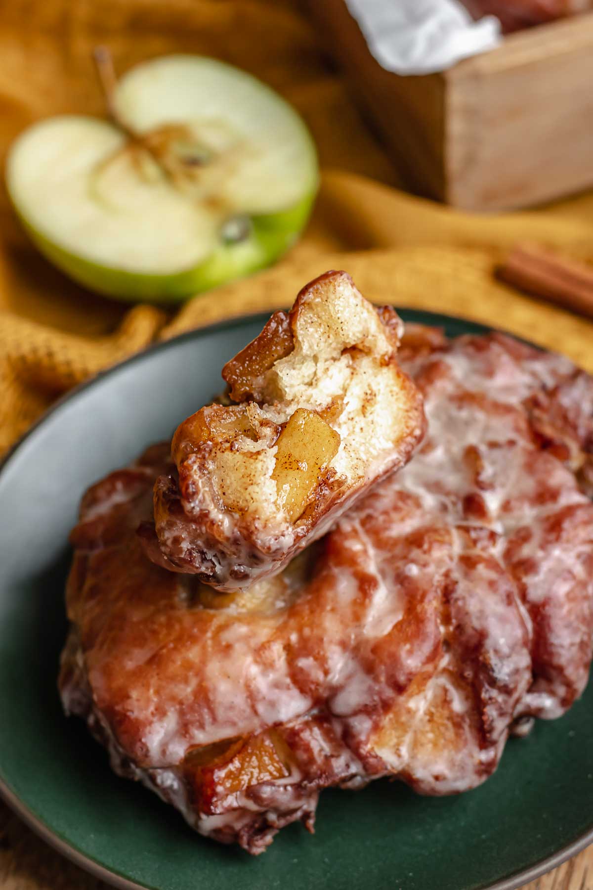 Apple fritter donuts on a plate. The top fritter it cut open.