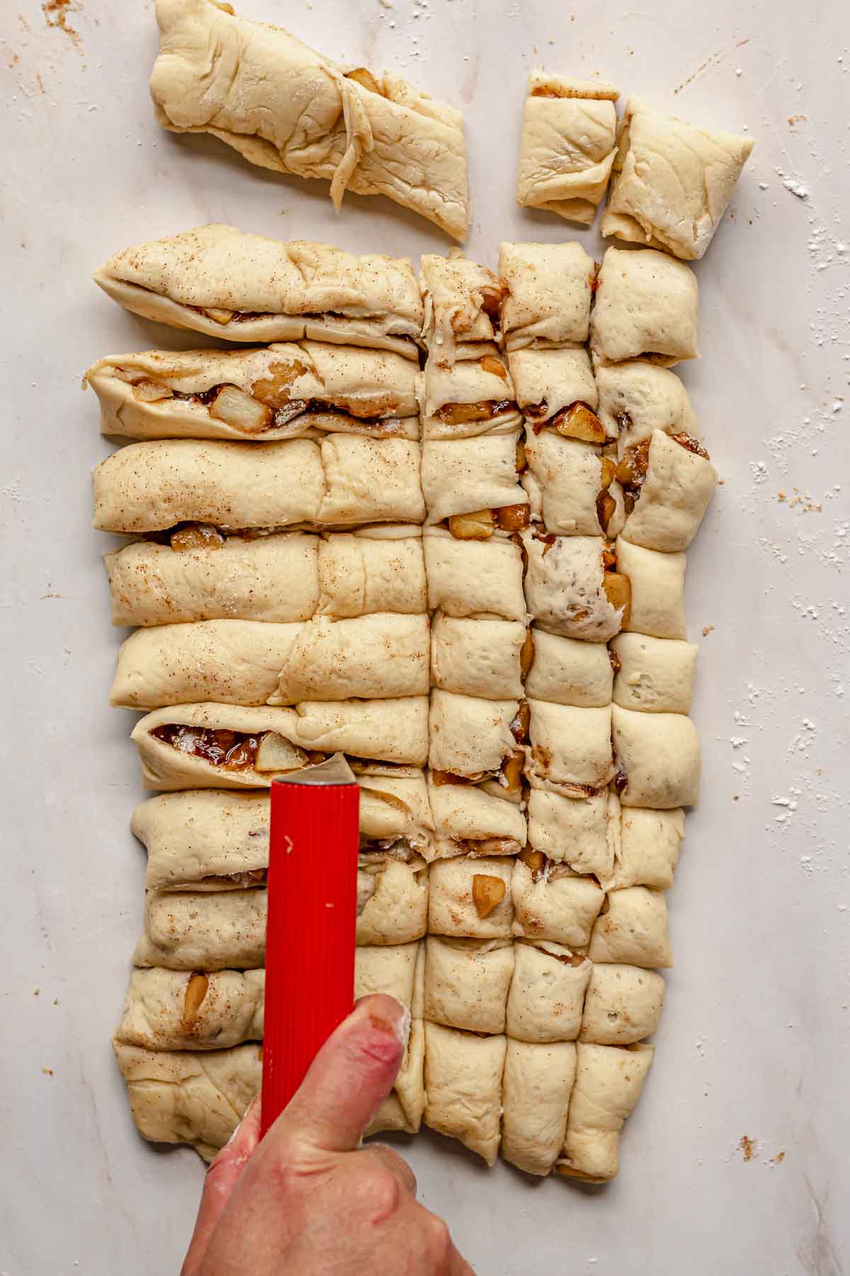 A bench scraper cuts the apple fritter donut dough into squares.