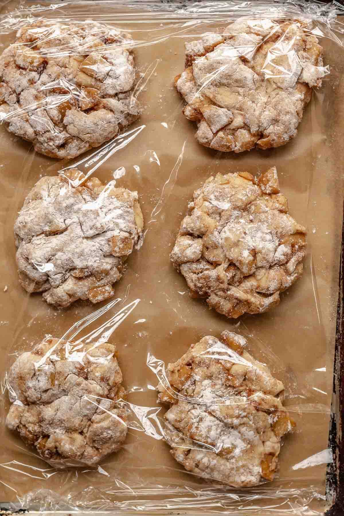 Apple fritters on a pan covered with plastic wrap.