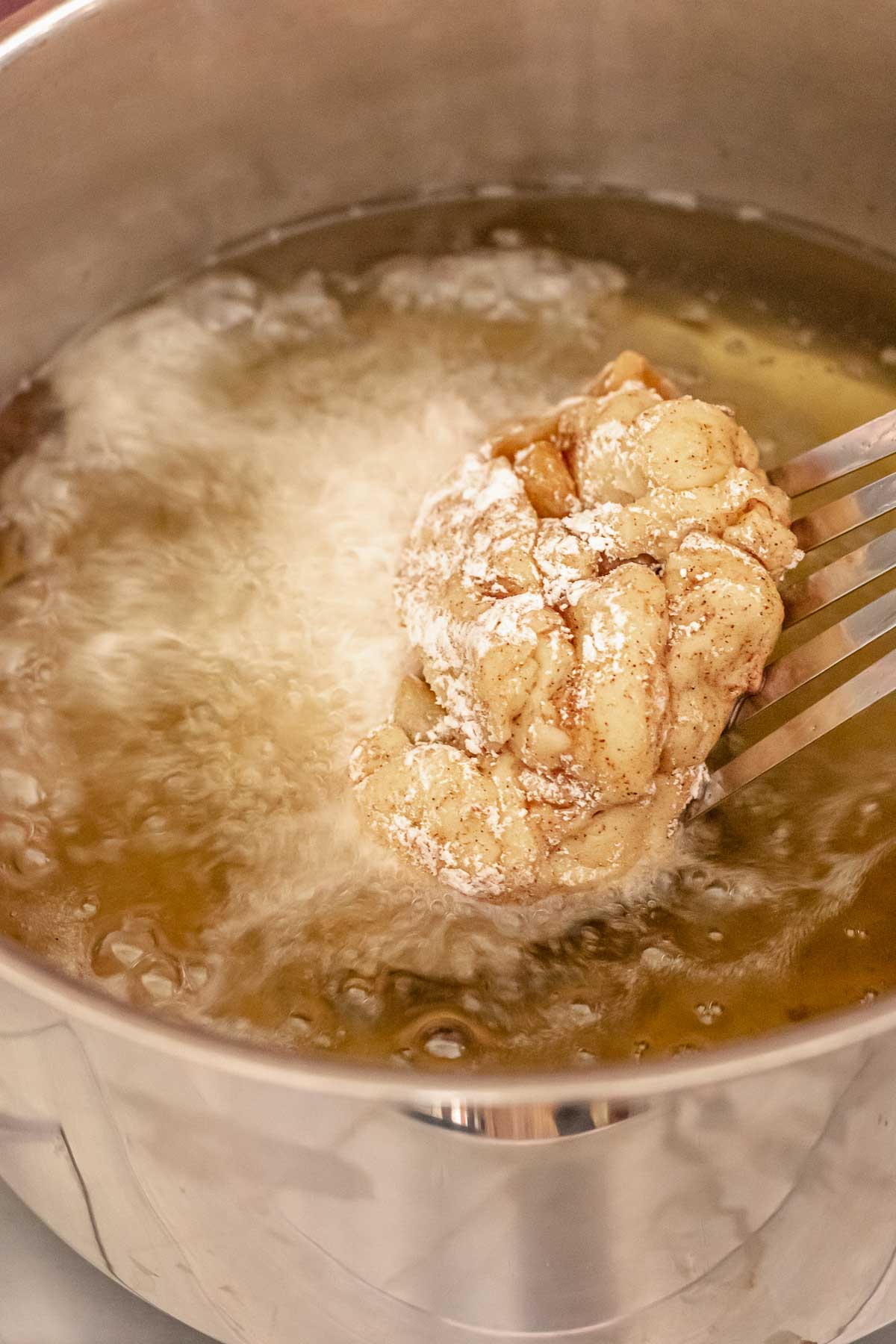 A spatula lowers an apple fritter donut into hot oil.