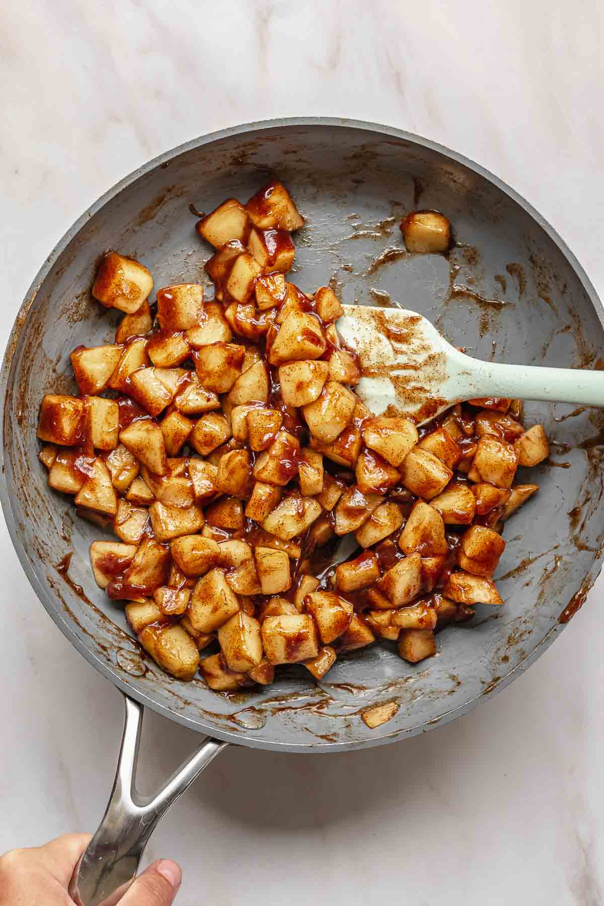 A spatula tosses spiced apples in a frying pan.