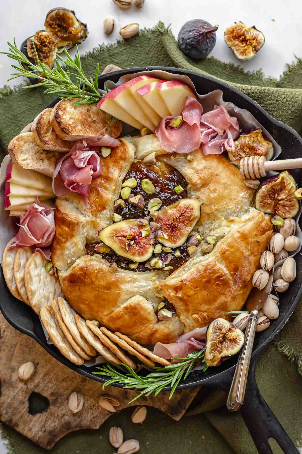 Finished baked brie in a cast iron skillet with dippers scattered around.