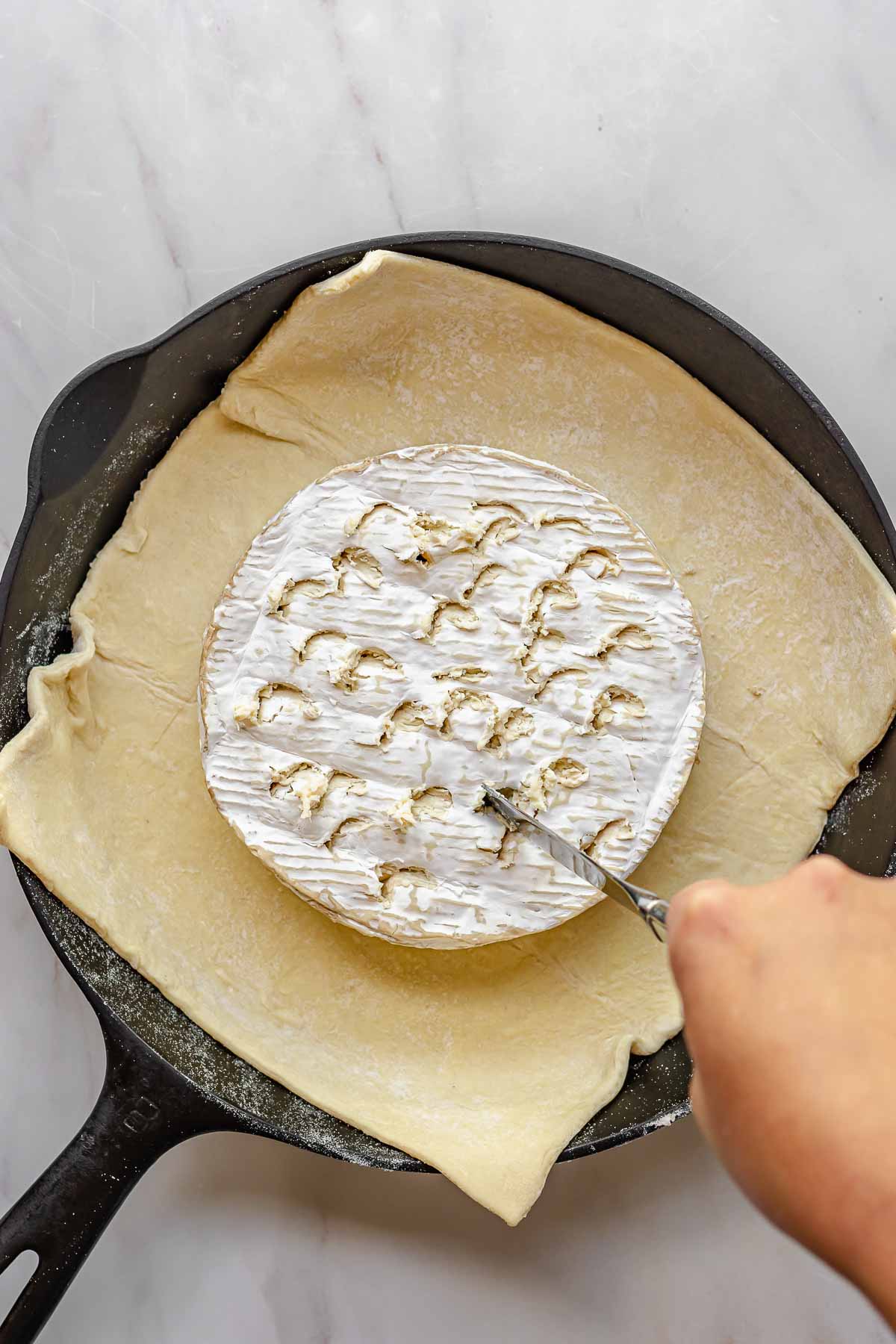 Brie on top of puff pastry and a knife cutting holes into the rind.