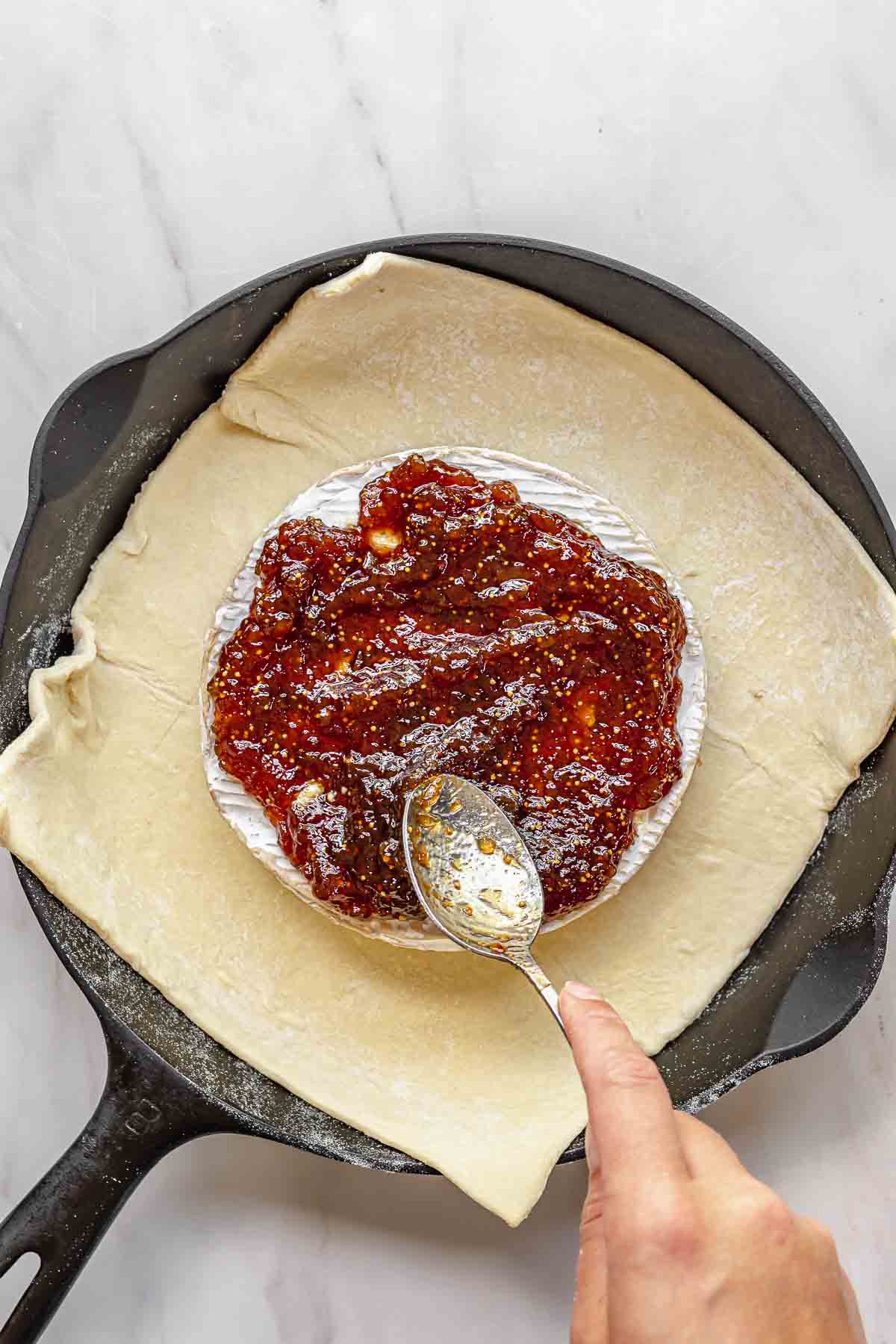 Fig jam being spread on top of brie with a spoon.
