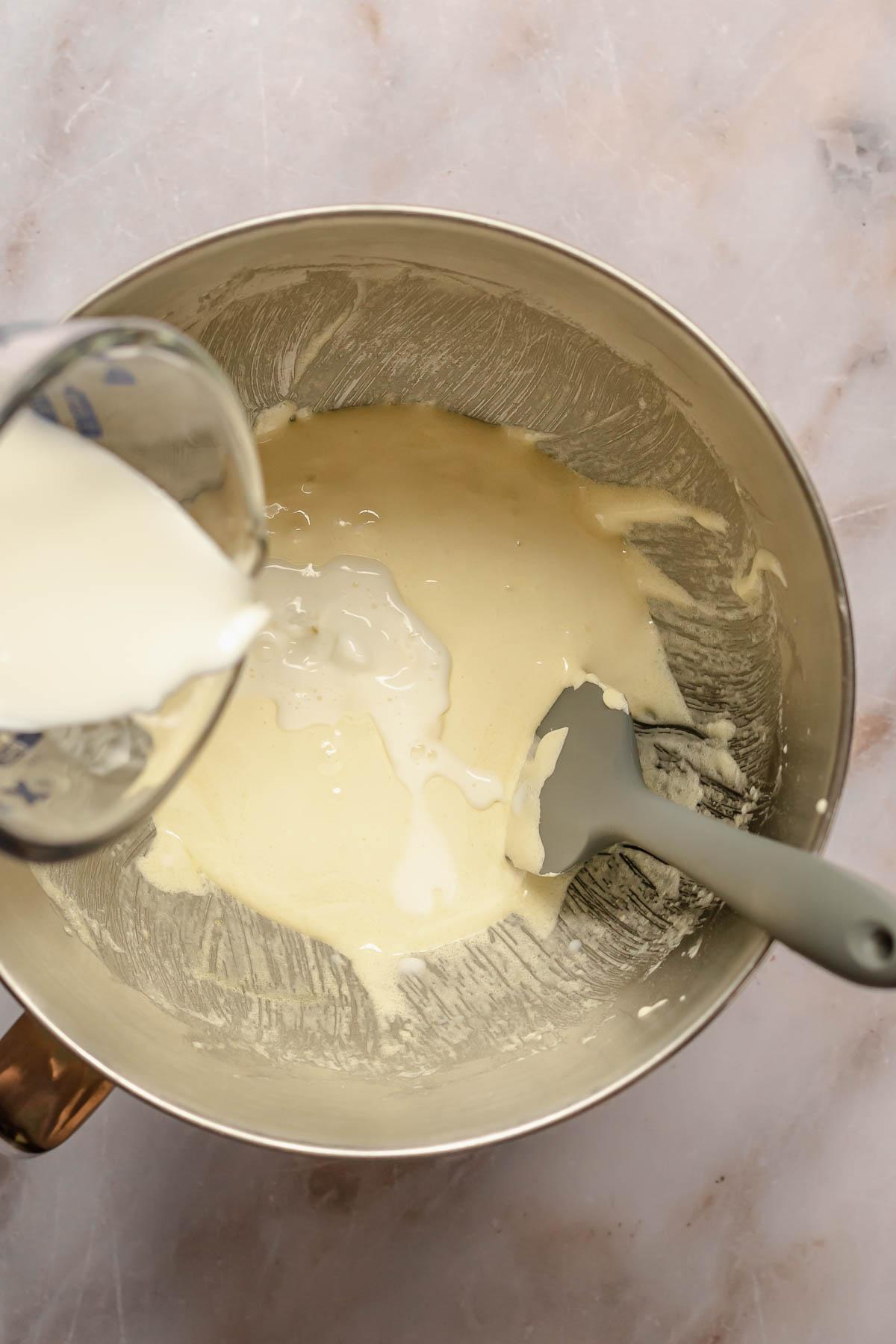Milk pouring into beaten egg yolks and sugar in a bowl.