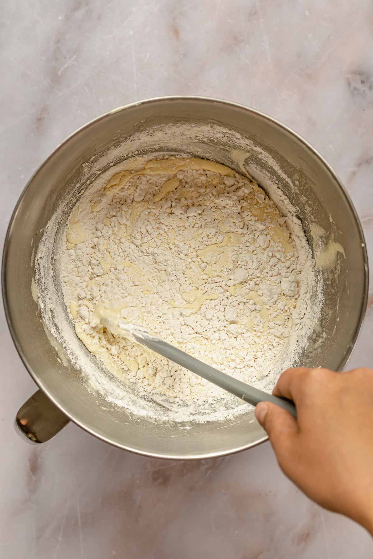 A hand and spatula folds flour into cake batter.