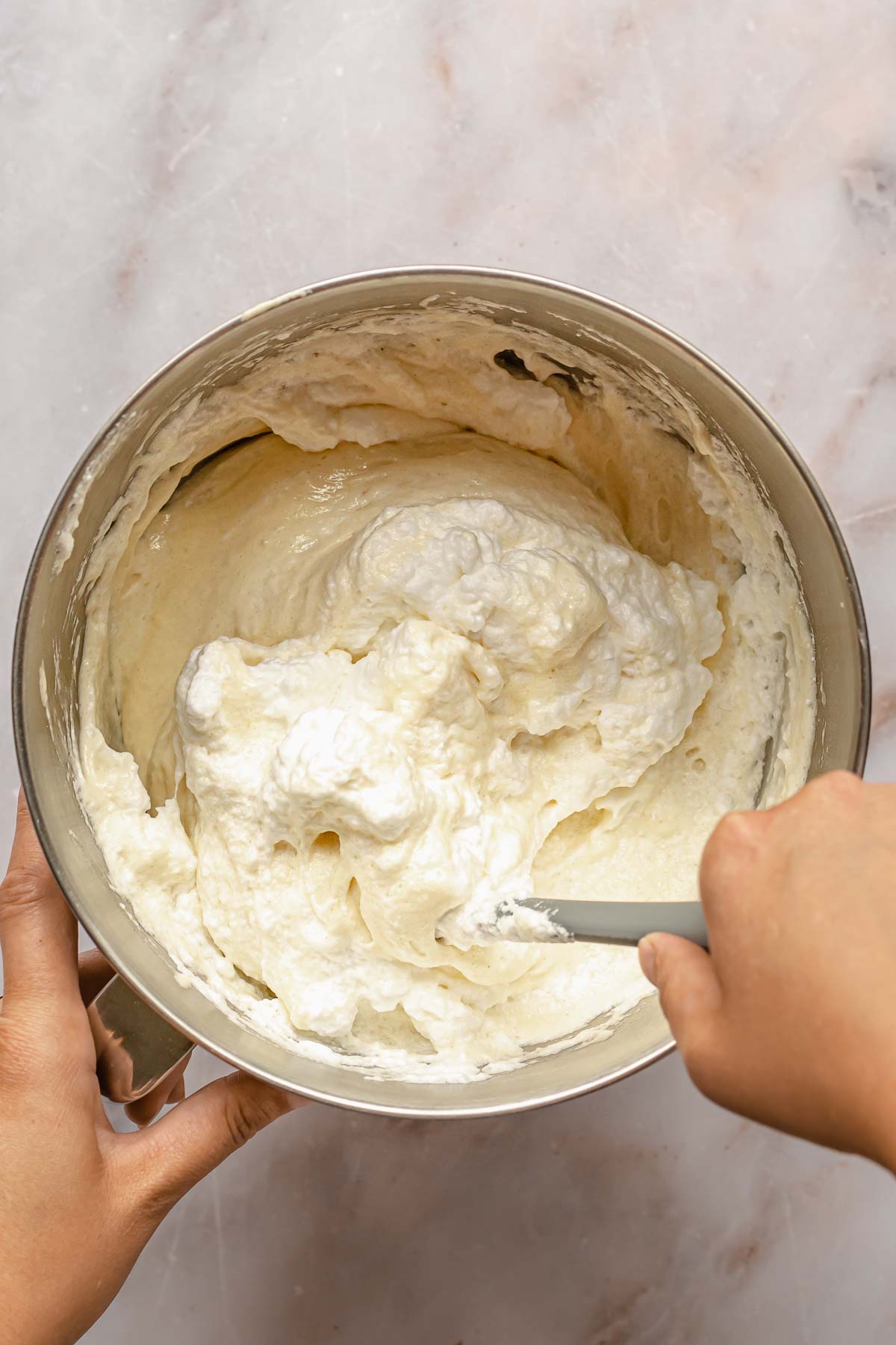 A hand folds whipped egg whites into cake batter.