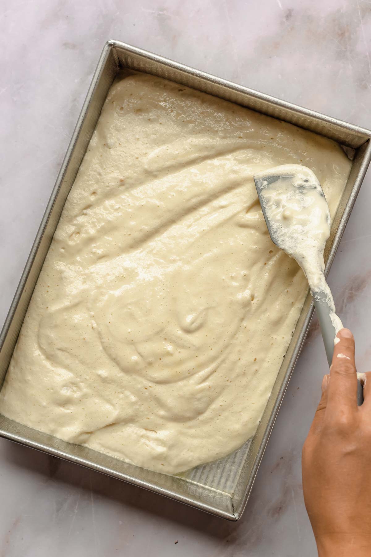 A spatula smooths cake batter into a large pan.