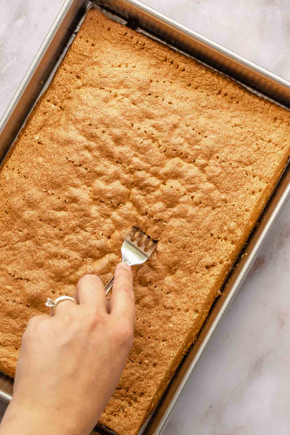A fork pricks holes into the baked sponge cake all over.