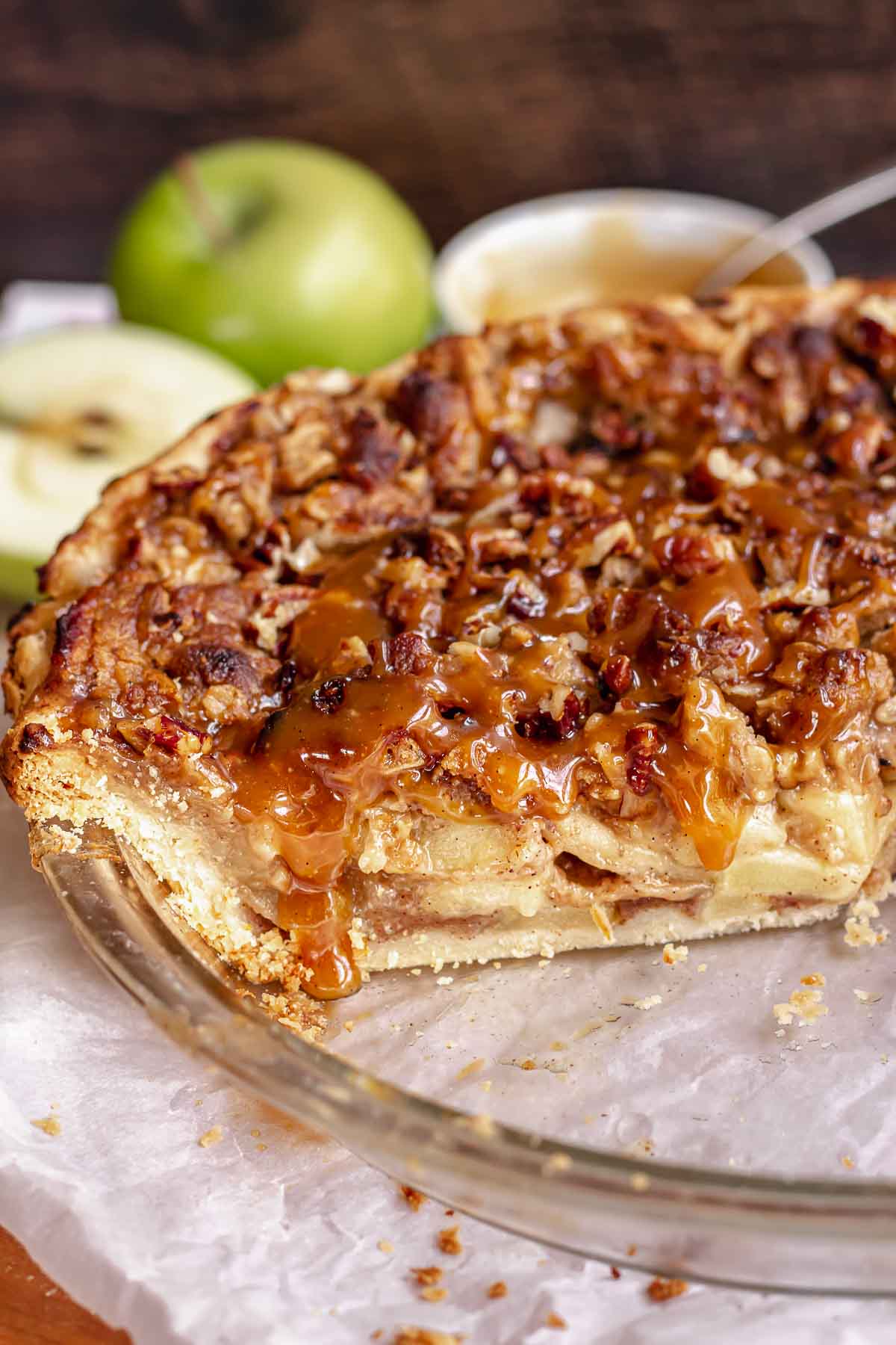 Caramel apple pie in a a pie dish with caramel drizzling over a cut slice.