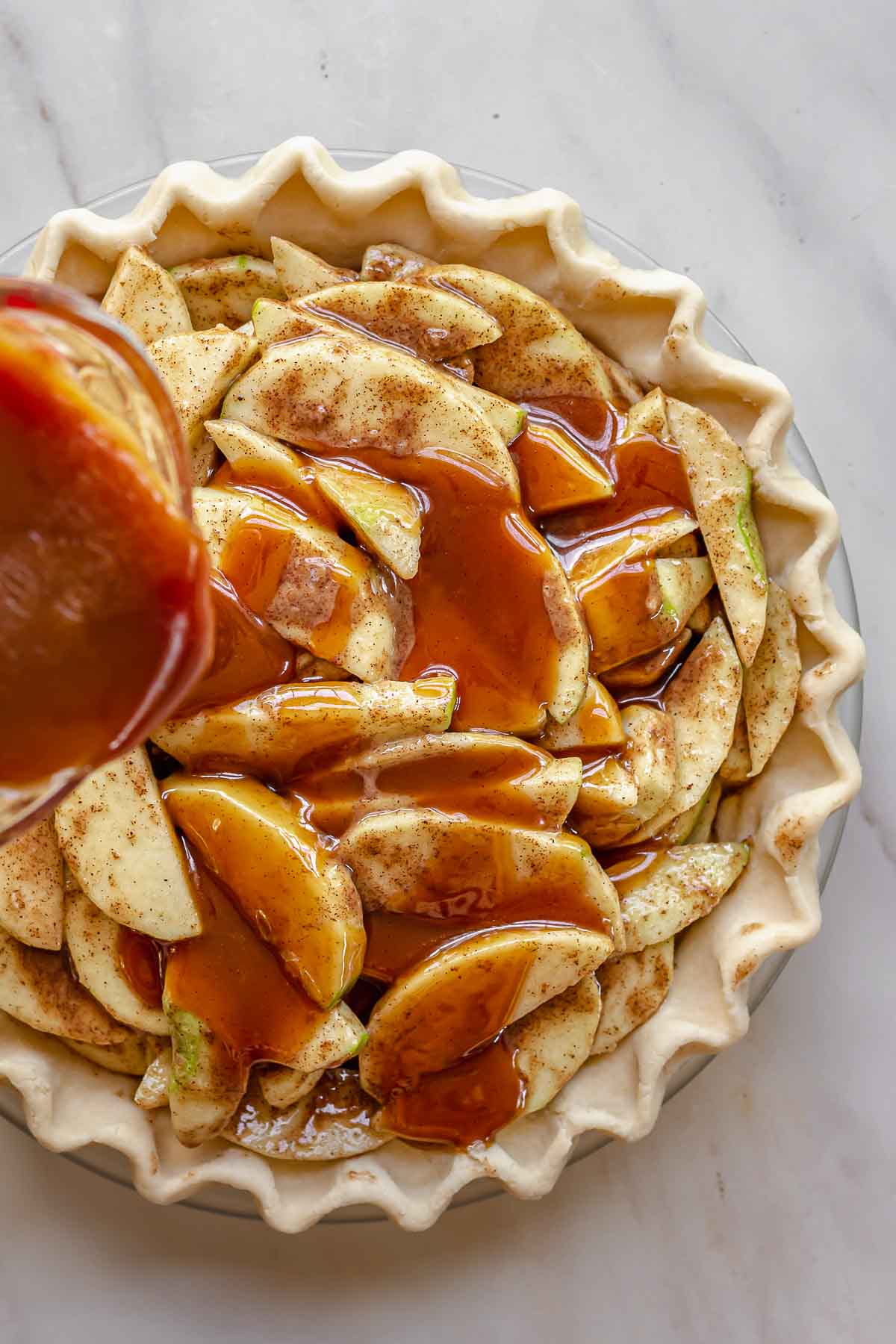 Salted caramel pouring over apples in a pie dish.