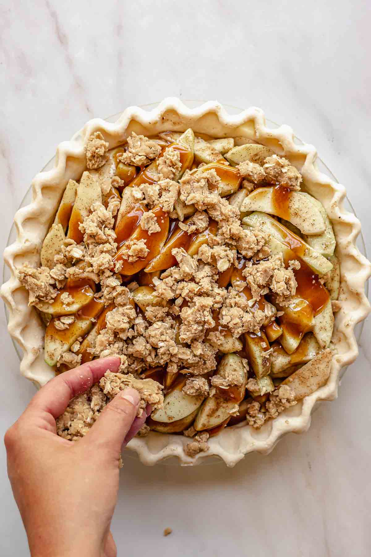 A hand adds crumb topping to the apples.