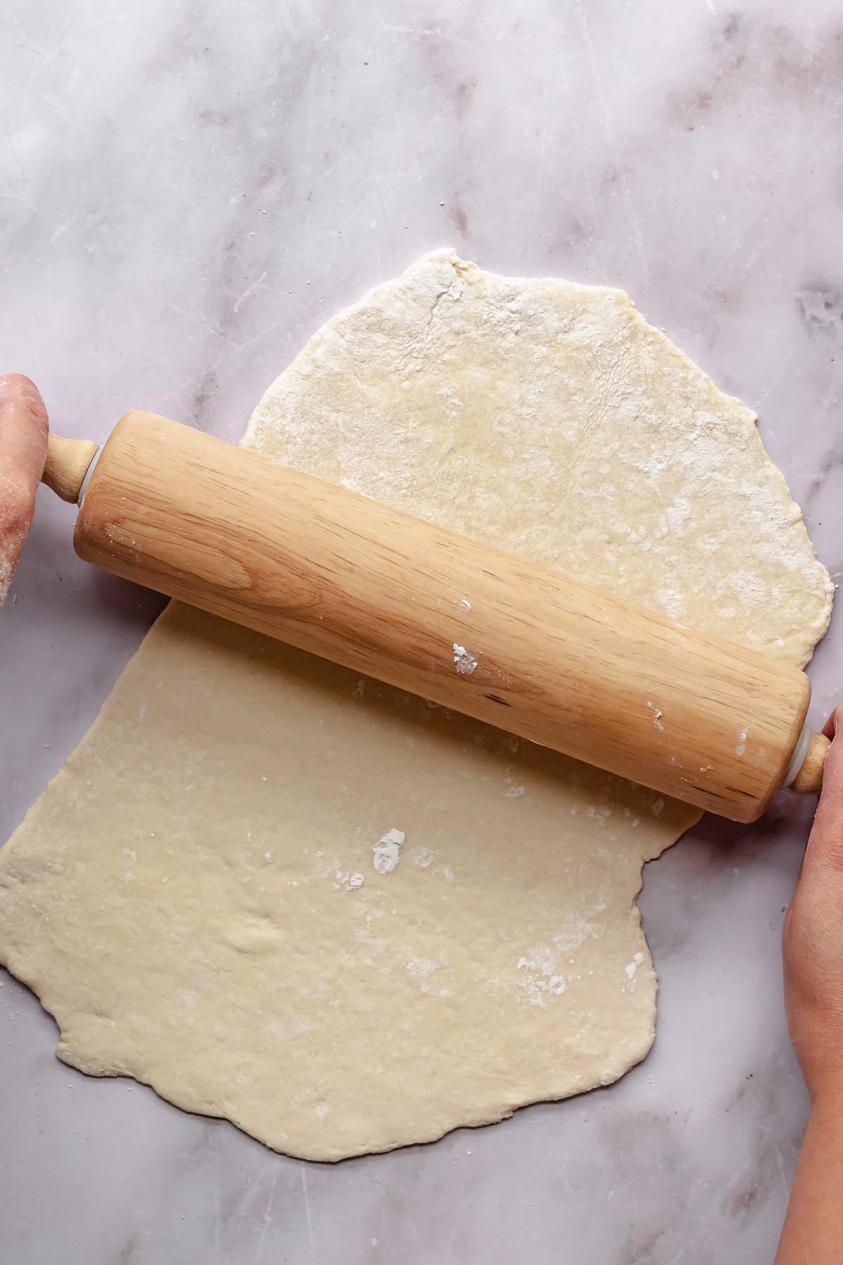 Hands using a rolling pin to roll noodle dough.