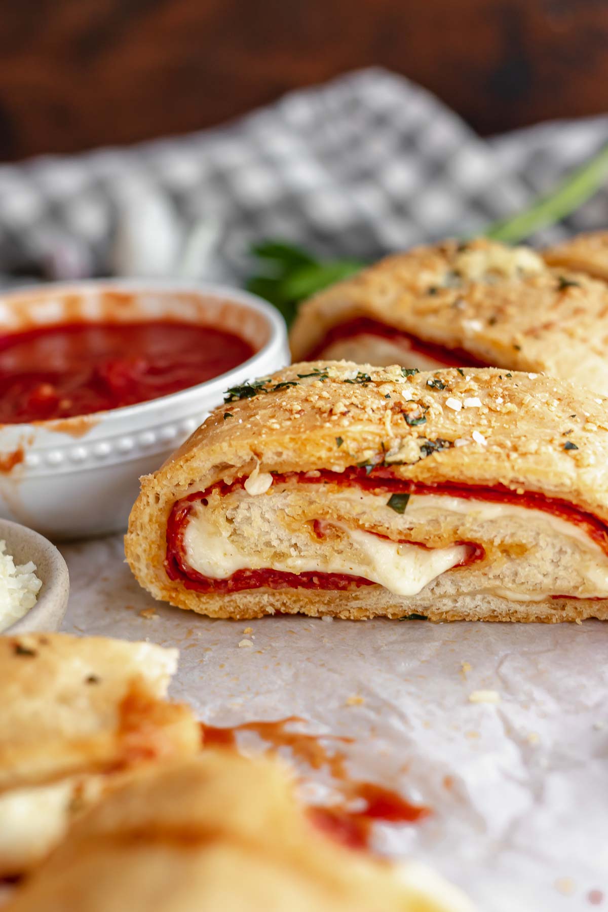 A slice of pepperoni roll with mozzarella coming out and marinara in the background.