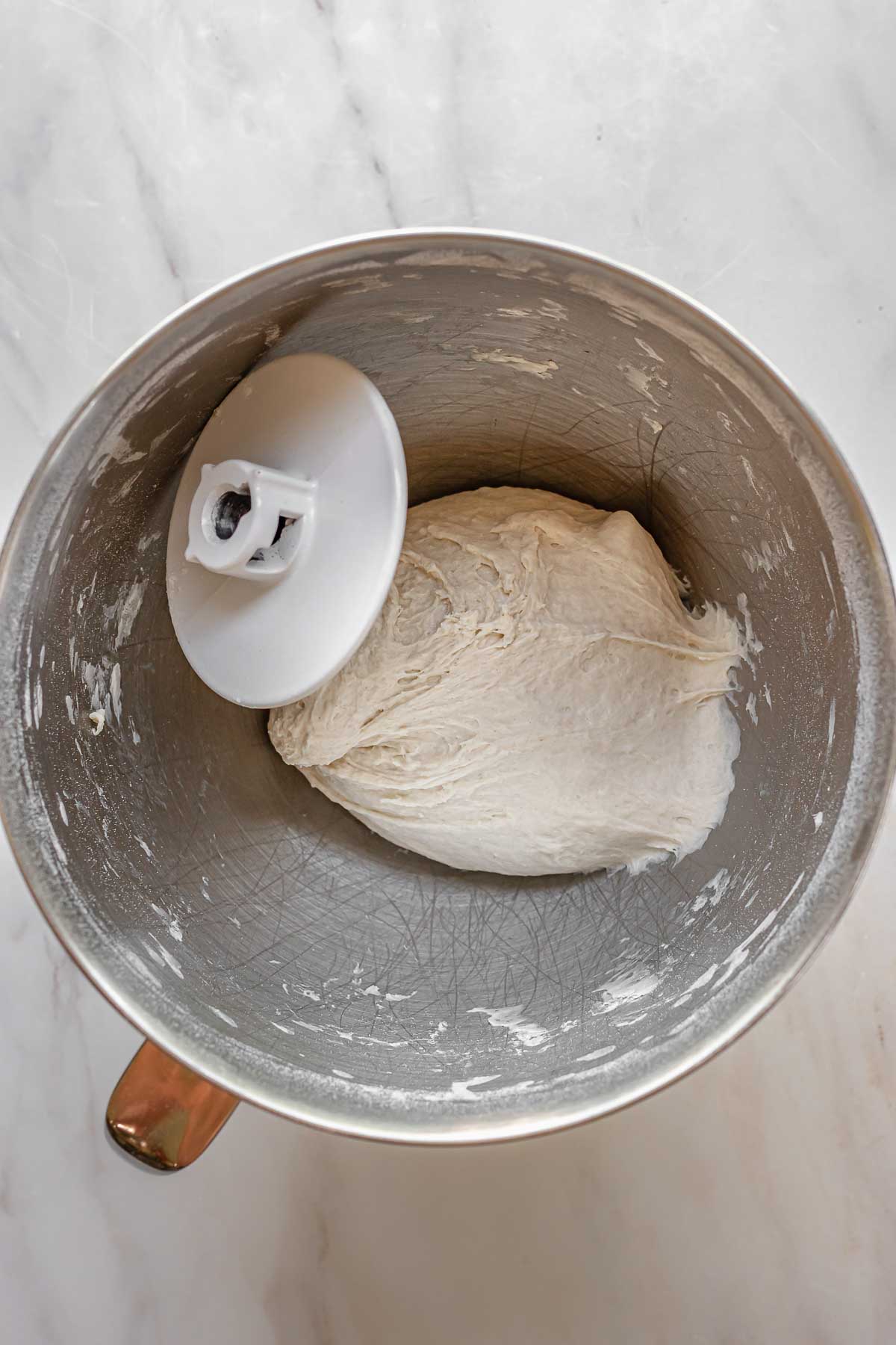 Pizza dough in the bowl of a stand mixer ready to rise.