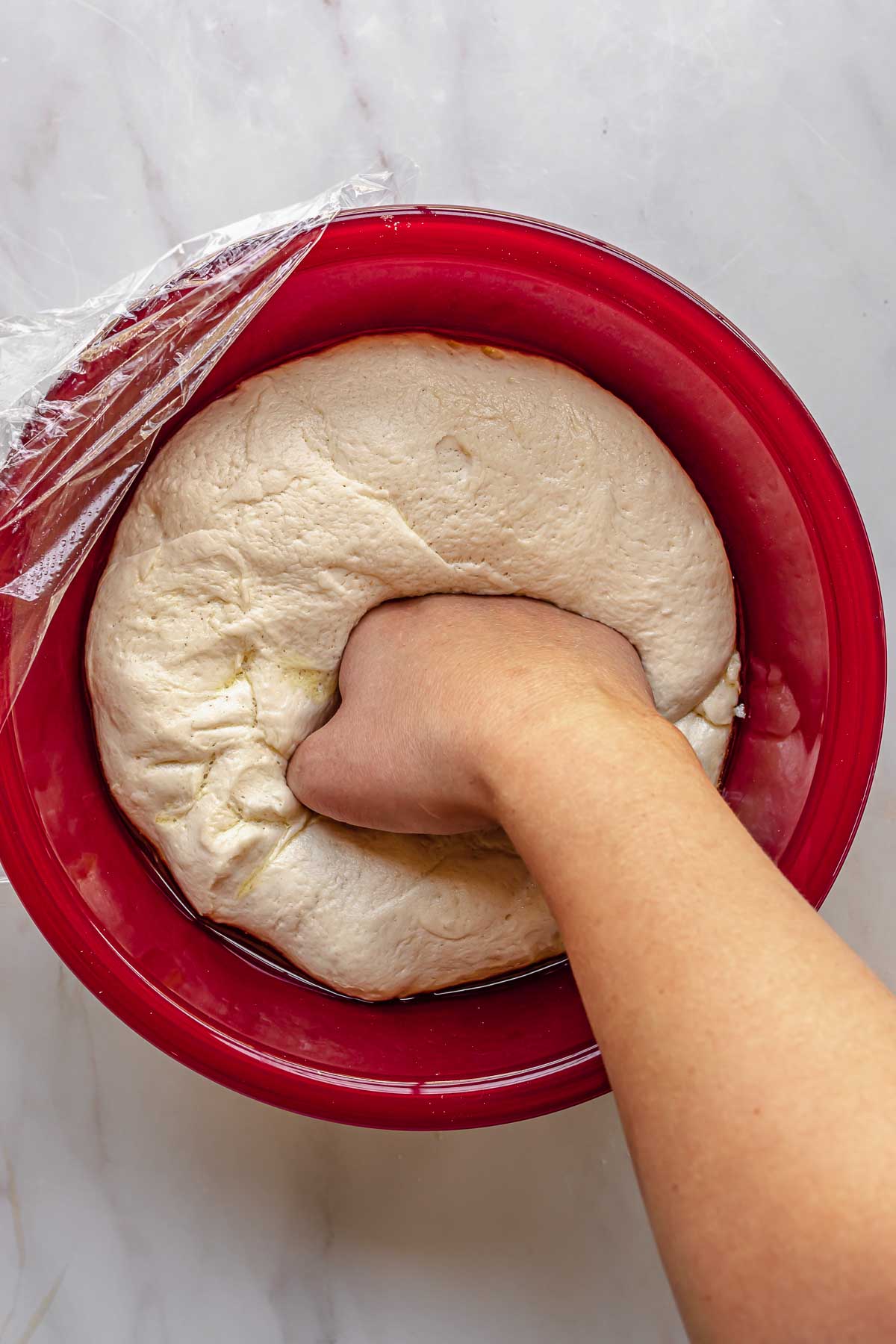 A hand punches down risen dough in a bowl.