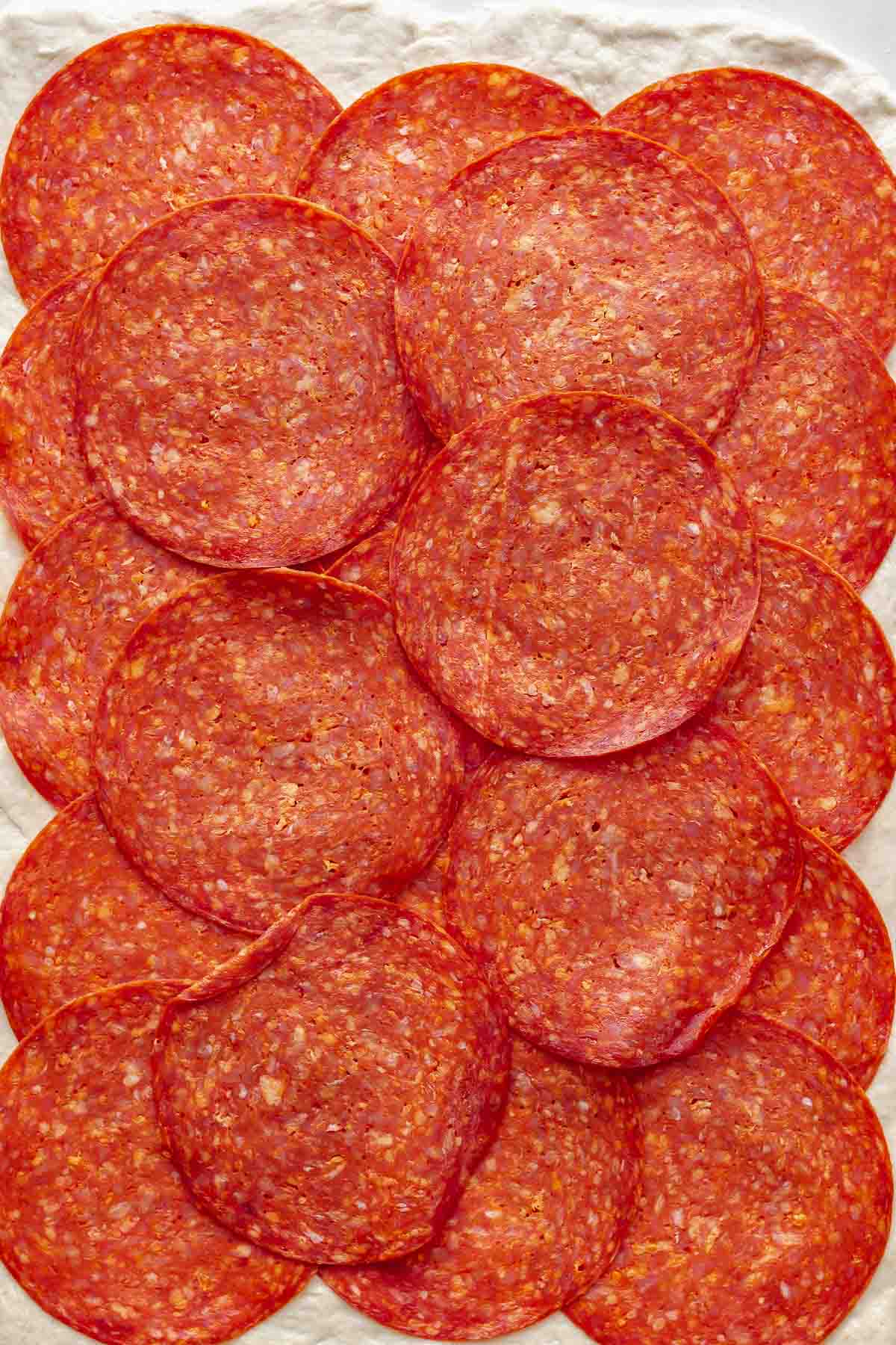 Sliced pepperoni lined up covering pizza dough.