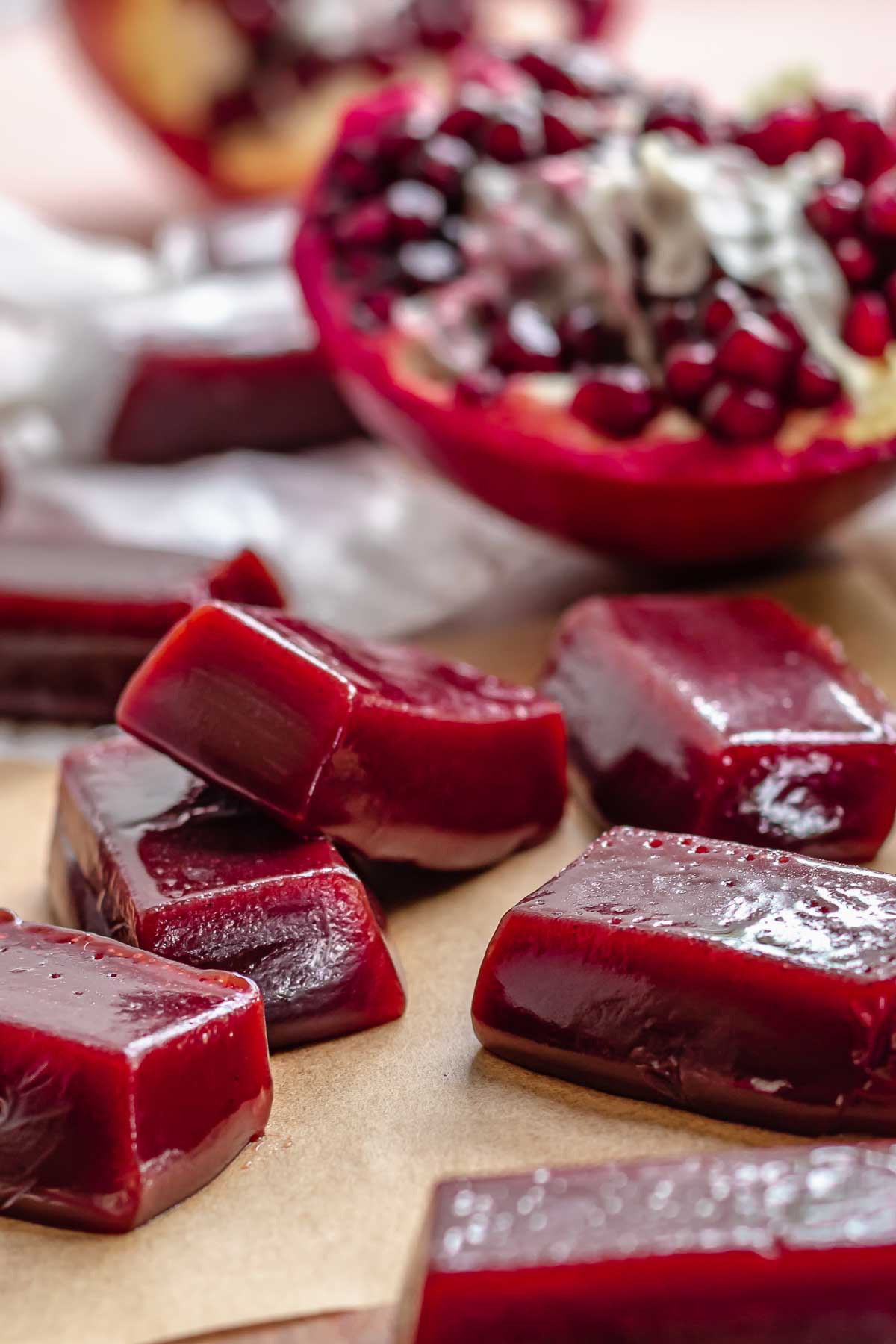 Pomegranate caramels layered on each other. A pomegranate is in the background.