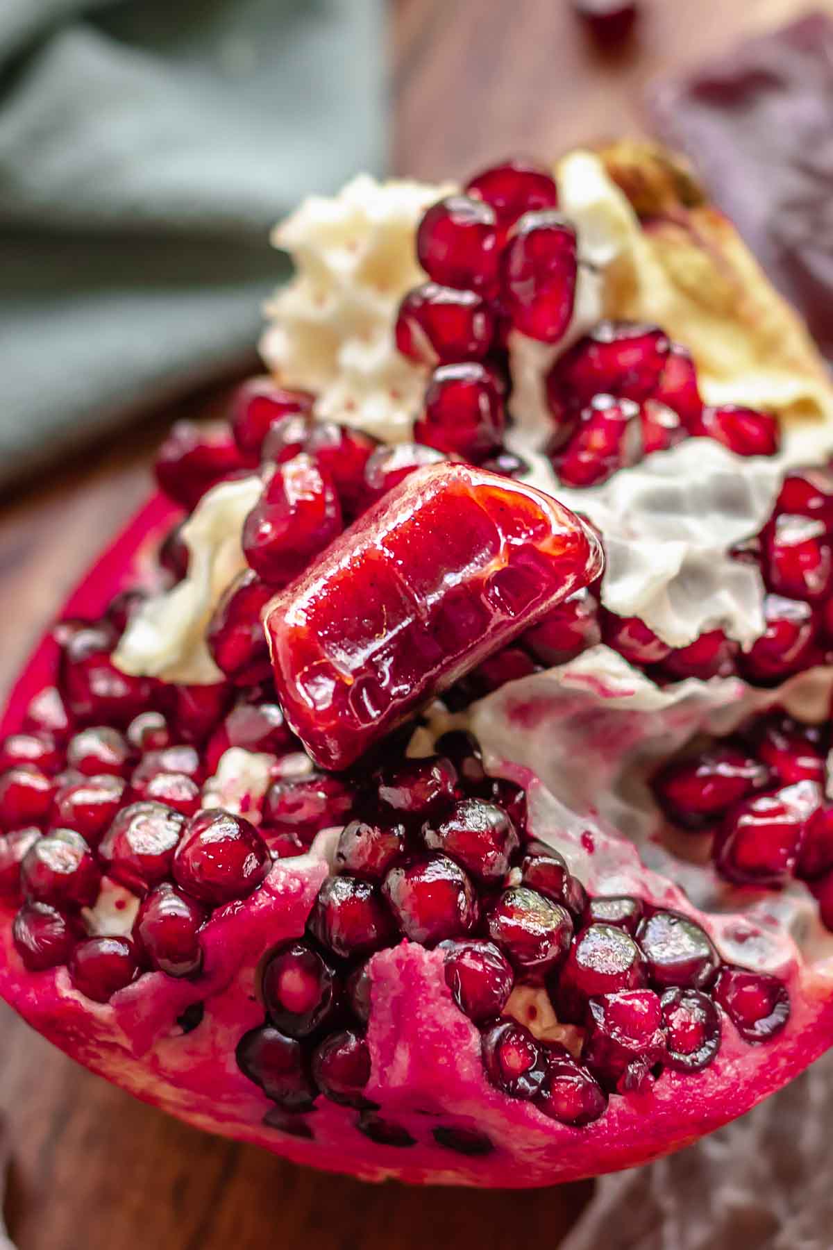 One piece of caramel with a bite removed sitting in pomegranate seeds.