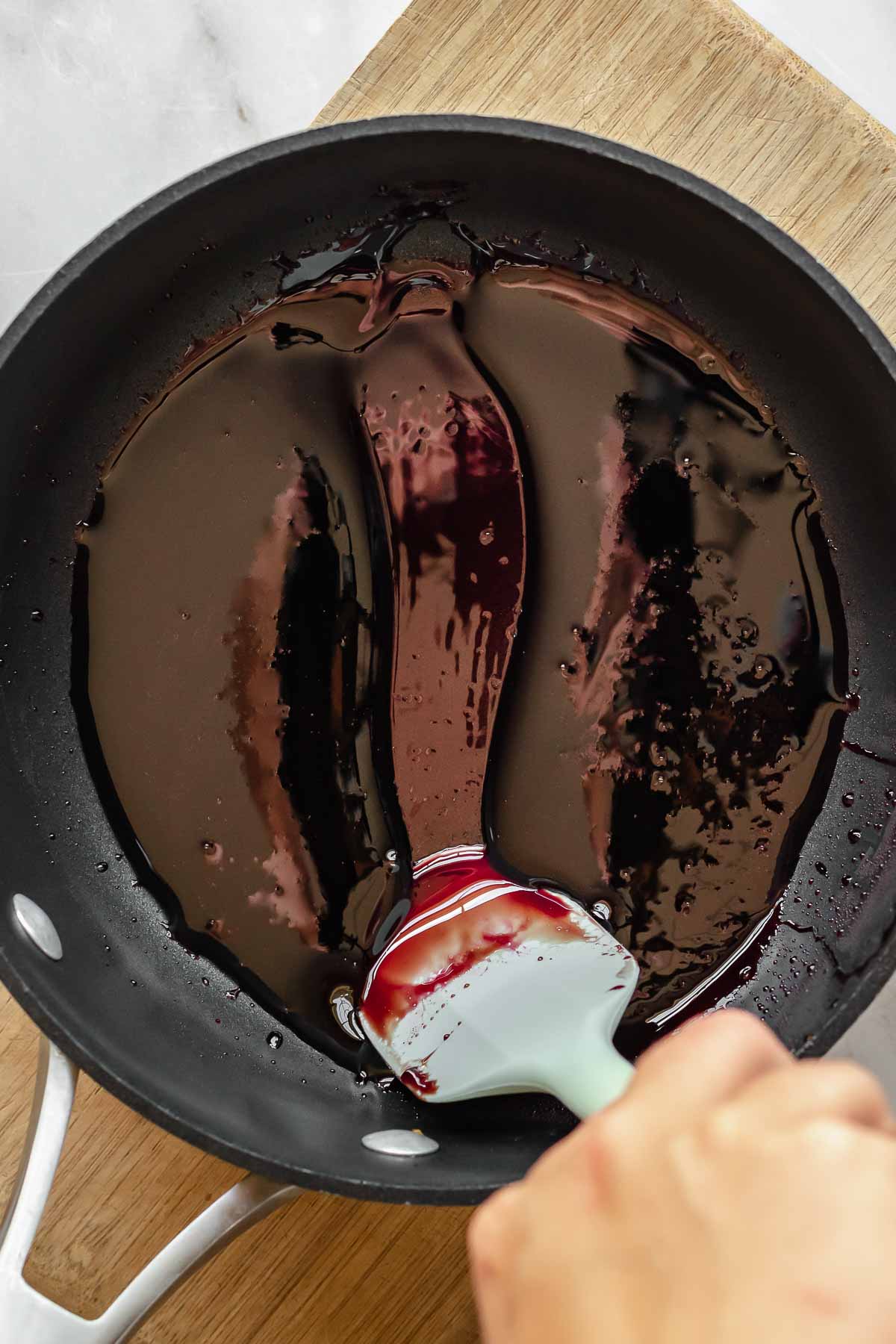 A spatula scrapes through pomegranate molasses in a pot.