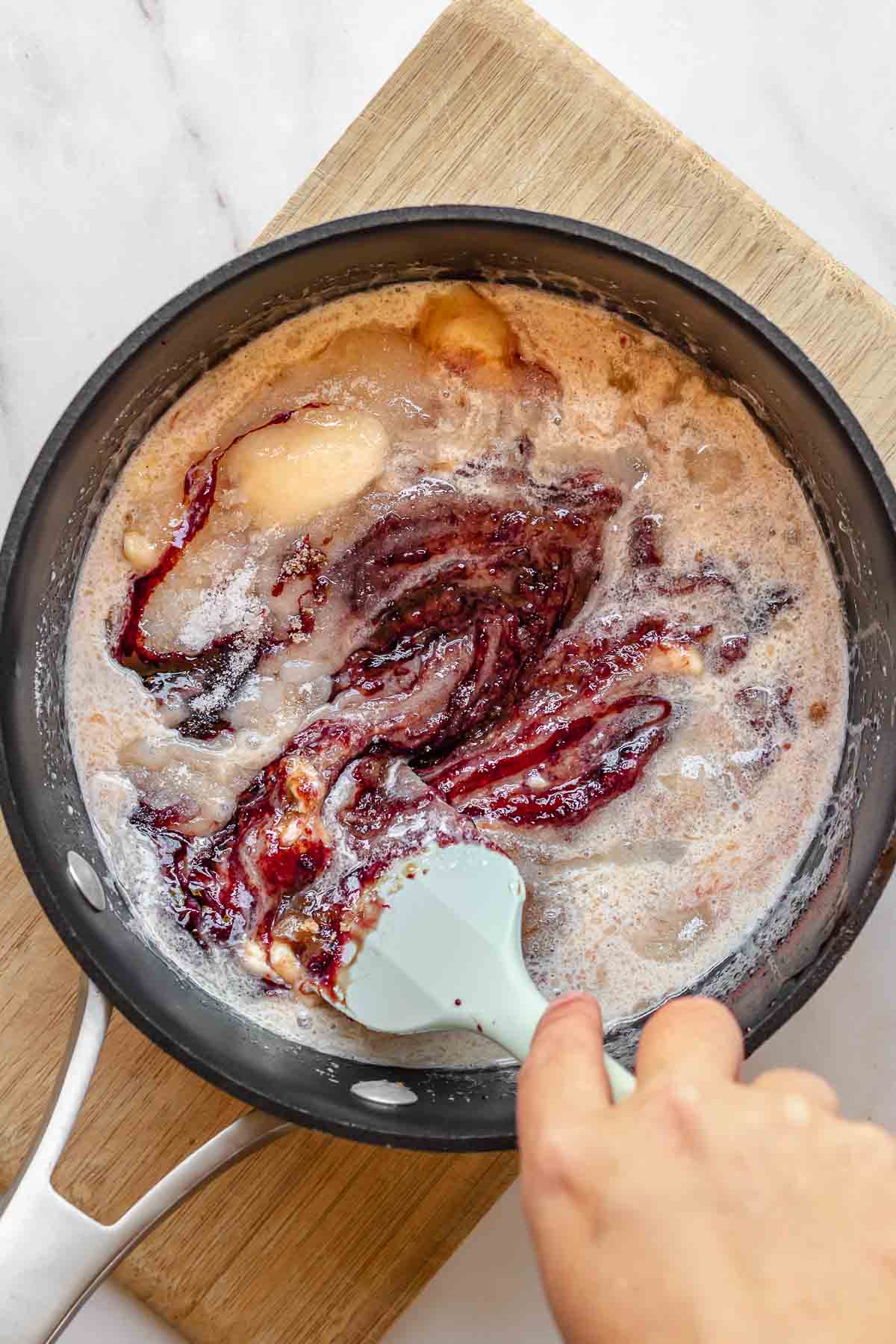 A spatula stirs butter, cream and sugar into pomegranate molasses.