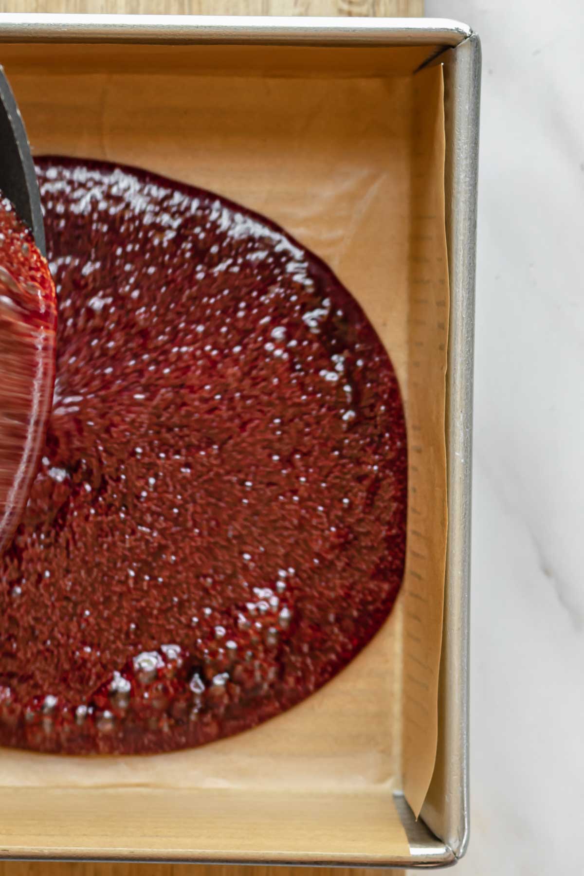 Pomegranate caramel in liquid form being poured into a prepared pan.