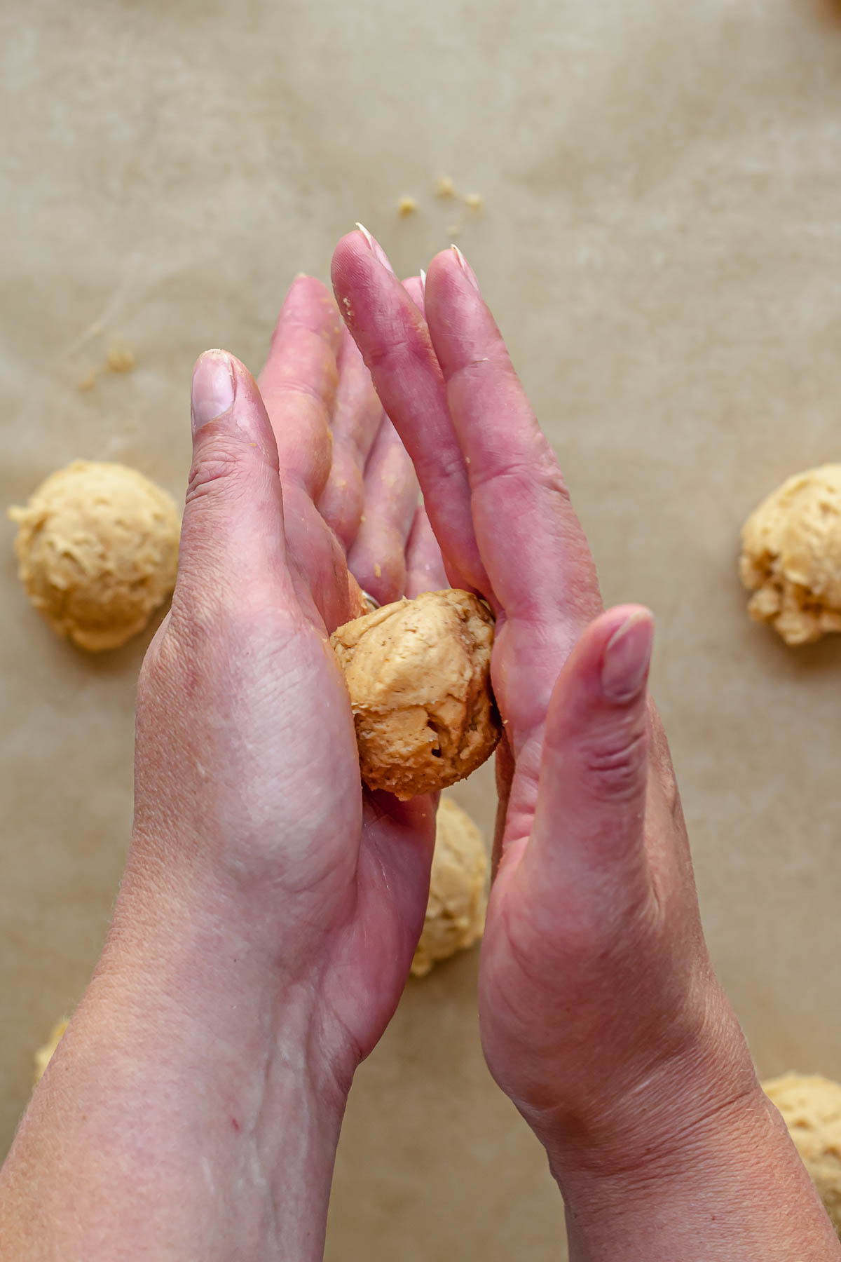 Hands rolling a pumpkin cookie dough into a ball.