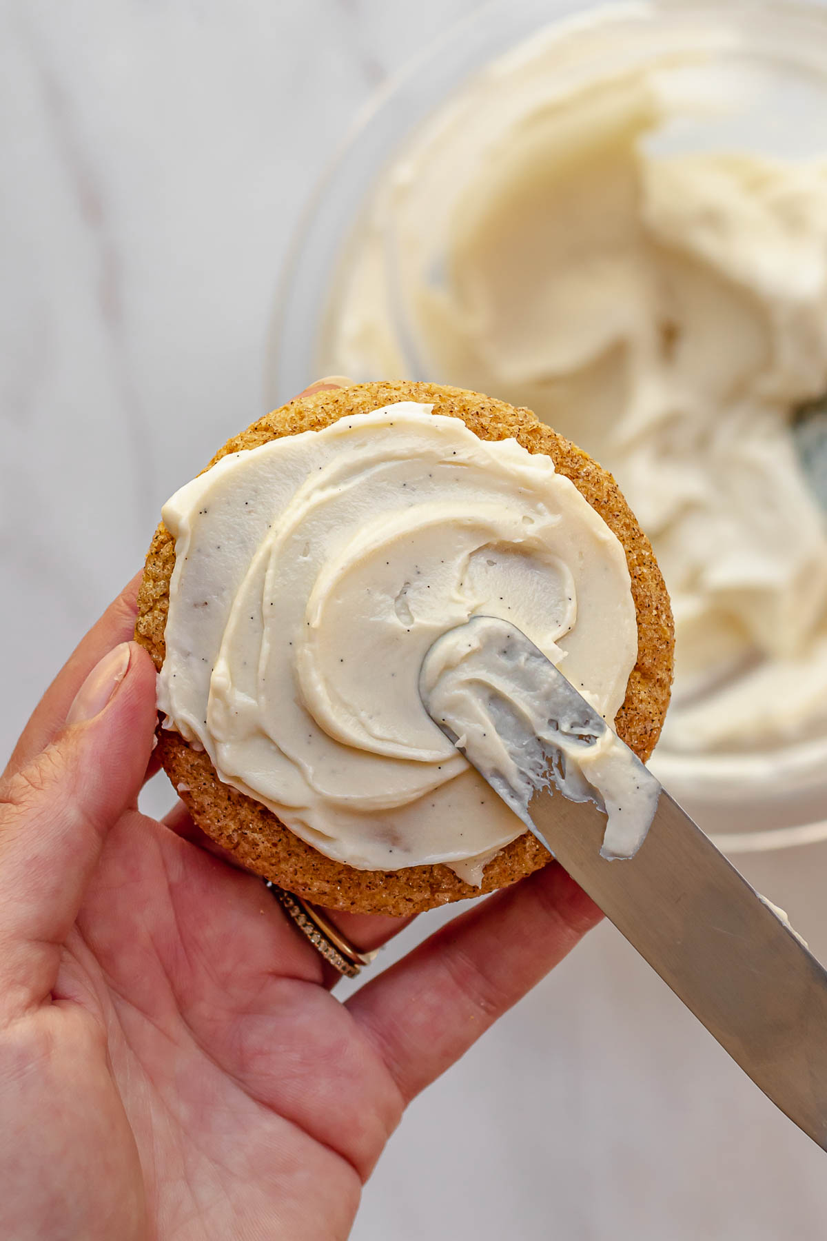 A rubber spatula swirls the cheesecake topping onto the cookie.
