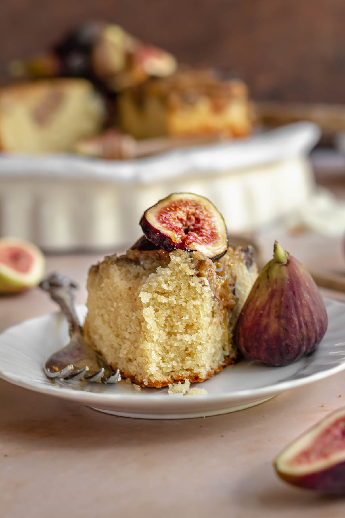 Fig cake on a plate with a fig on top and fork next to it. A bite is removed.