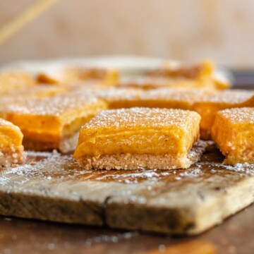 Pumpkin gooey bars on a cutting board cut apart and dusted with powdered sugar.