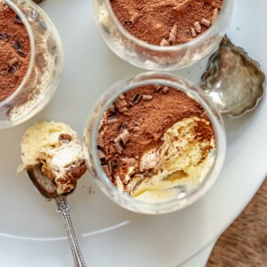 Tiramisu cups on a platter. One has a bite removed sitting on a spoon.