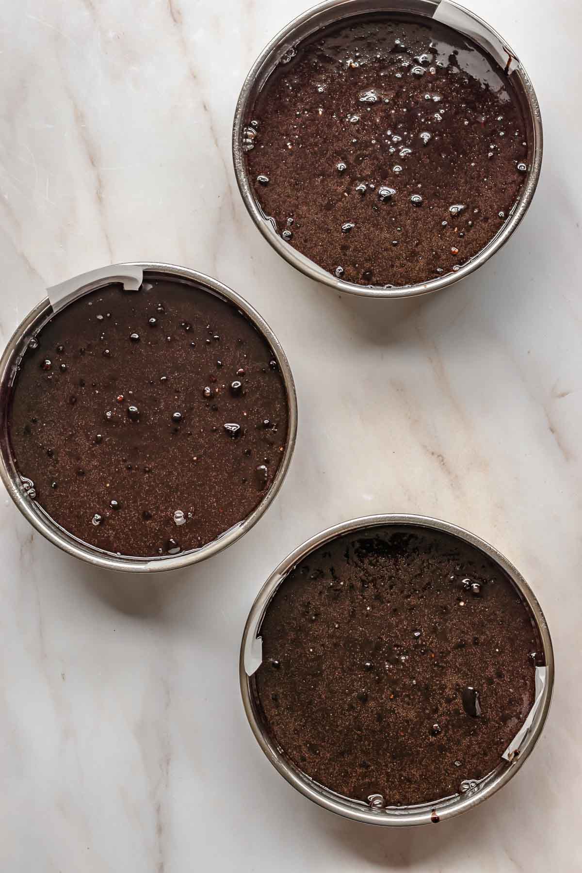 Chocolate cake batter in three cake pans.
