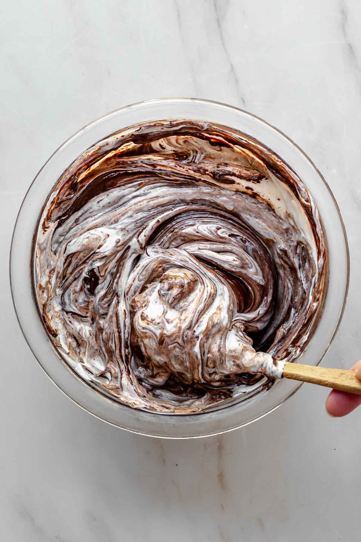 A hand mixes melted chocolate and sour cream in a bowl.