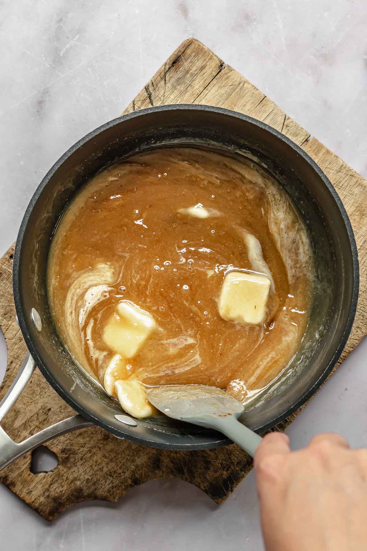 A spatula stirs butter into a pot.