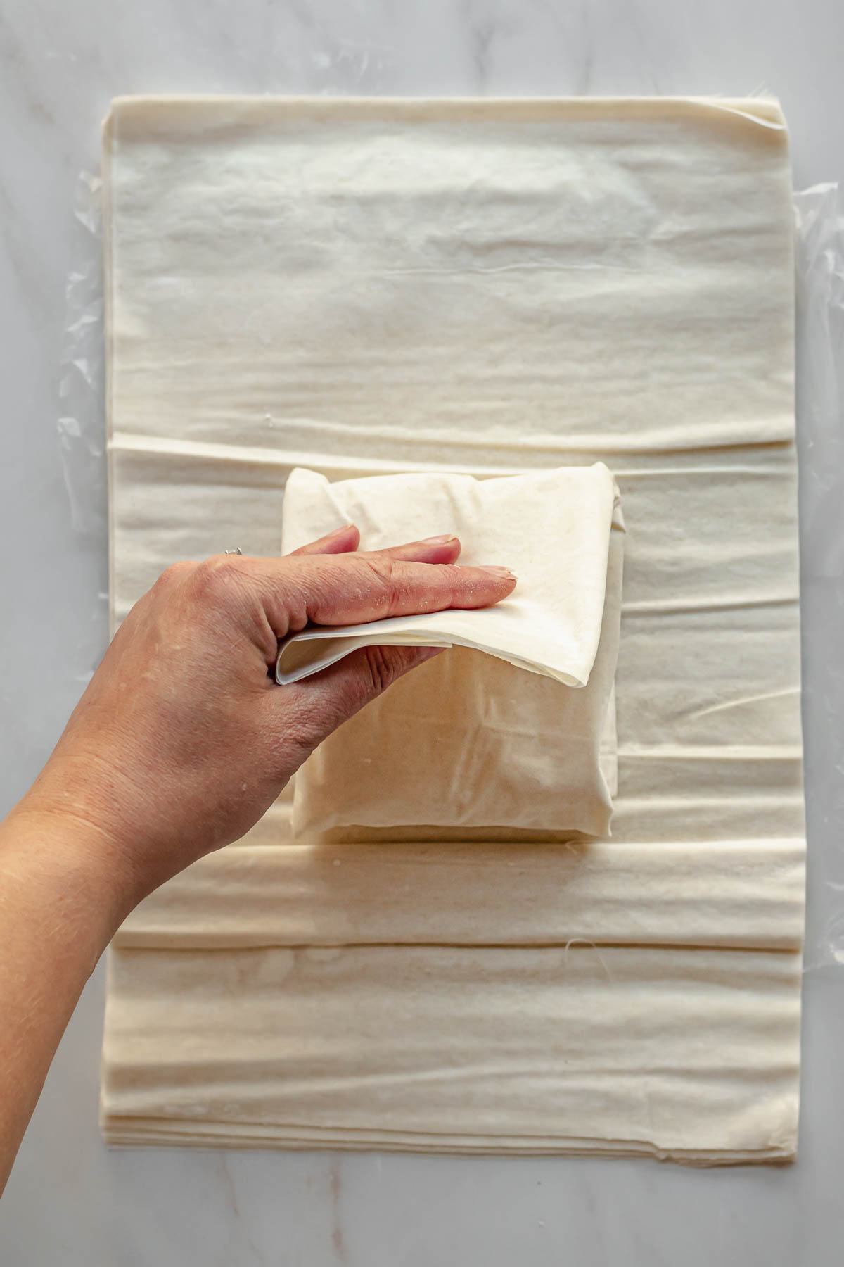 A hand folds phyllo pastry over feta cheese.