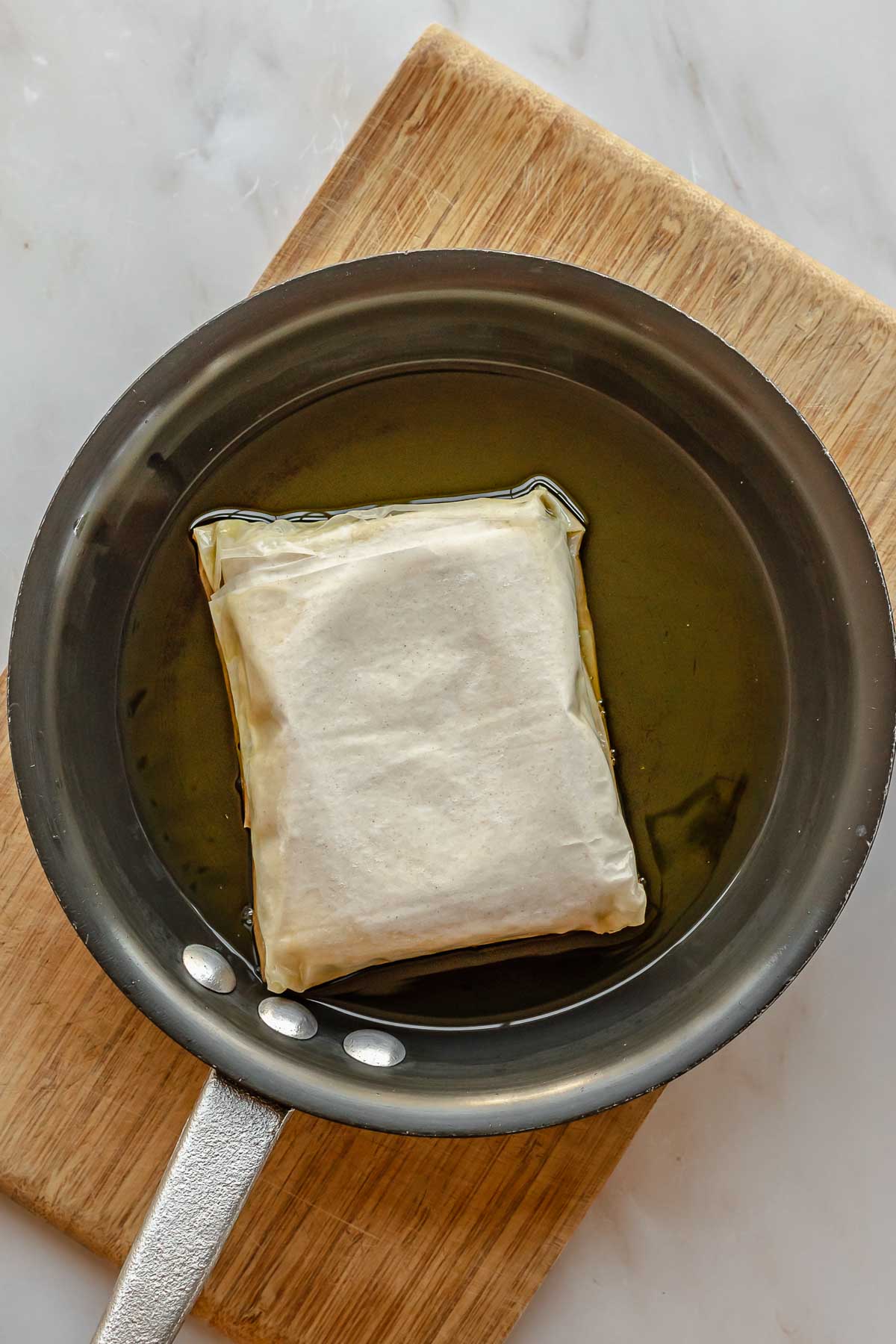 A block of phyllo wrapped feta in a pan of olive oil.