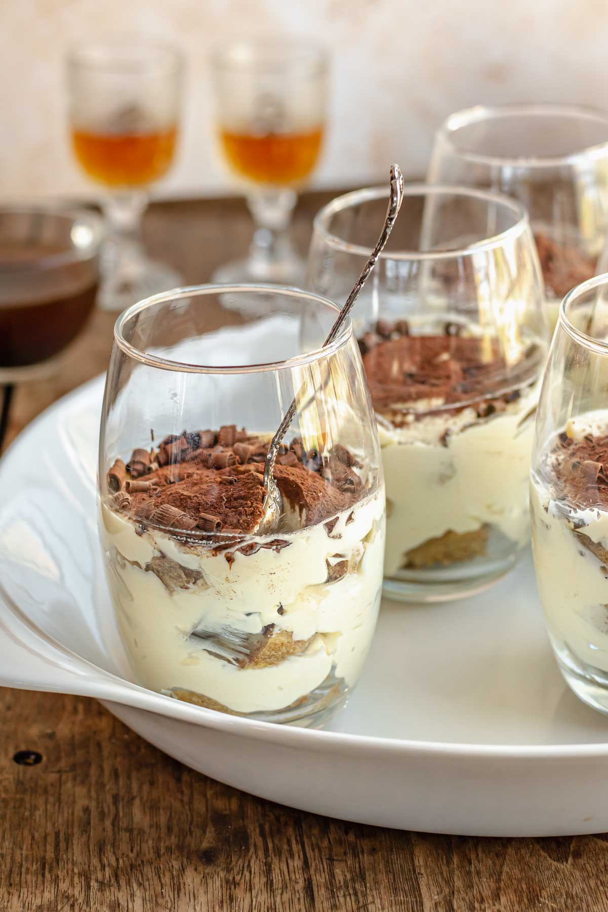Tiramisu cups on a platter. Rum in glasses sit in the background.